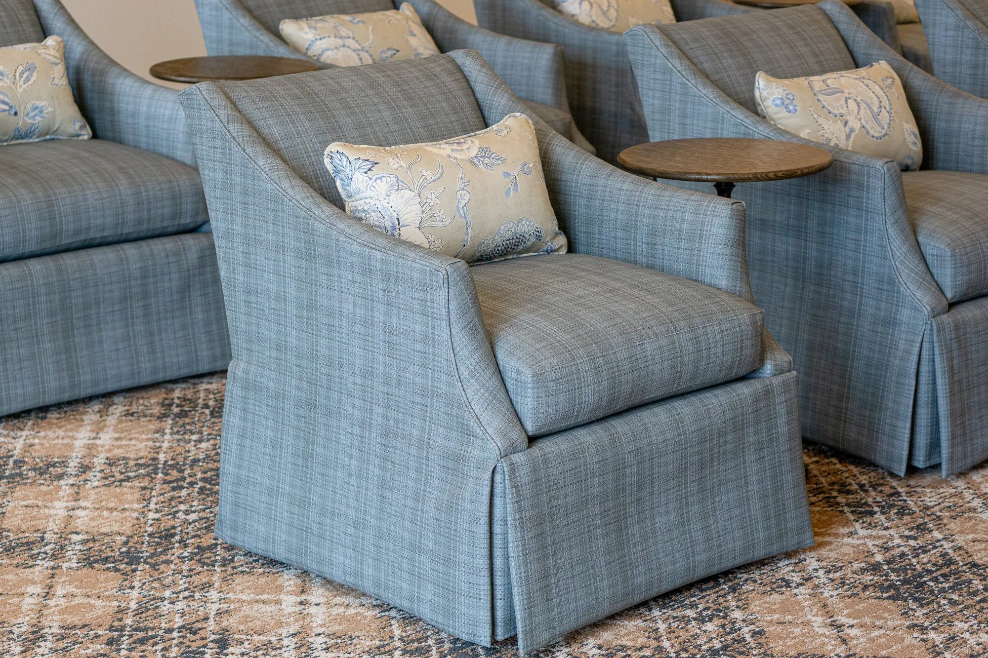Senior living interior detail: skirted blue plaid armchairs with floral pillows and small round drink tables