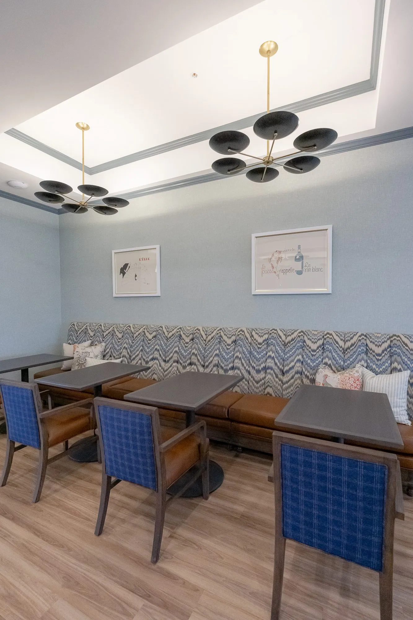 Senior living dining room with a chevron upholstered banquette and blue plaid chairs under black disc pendants