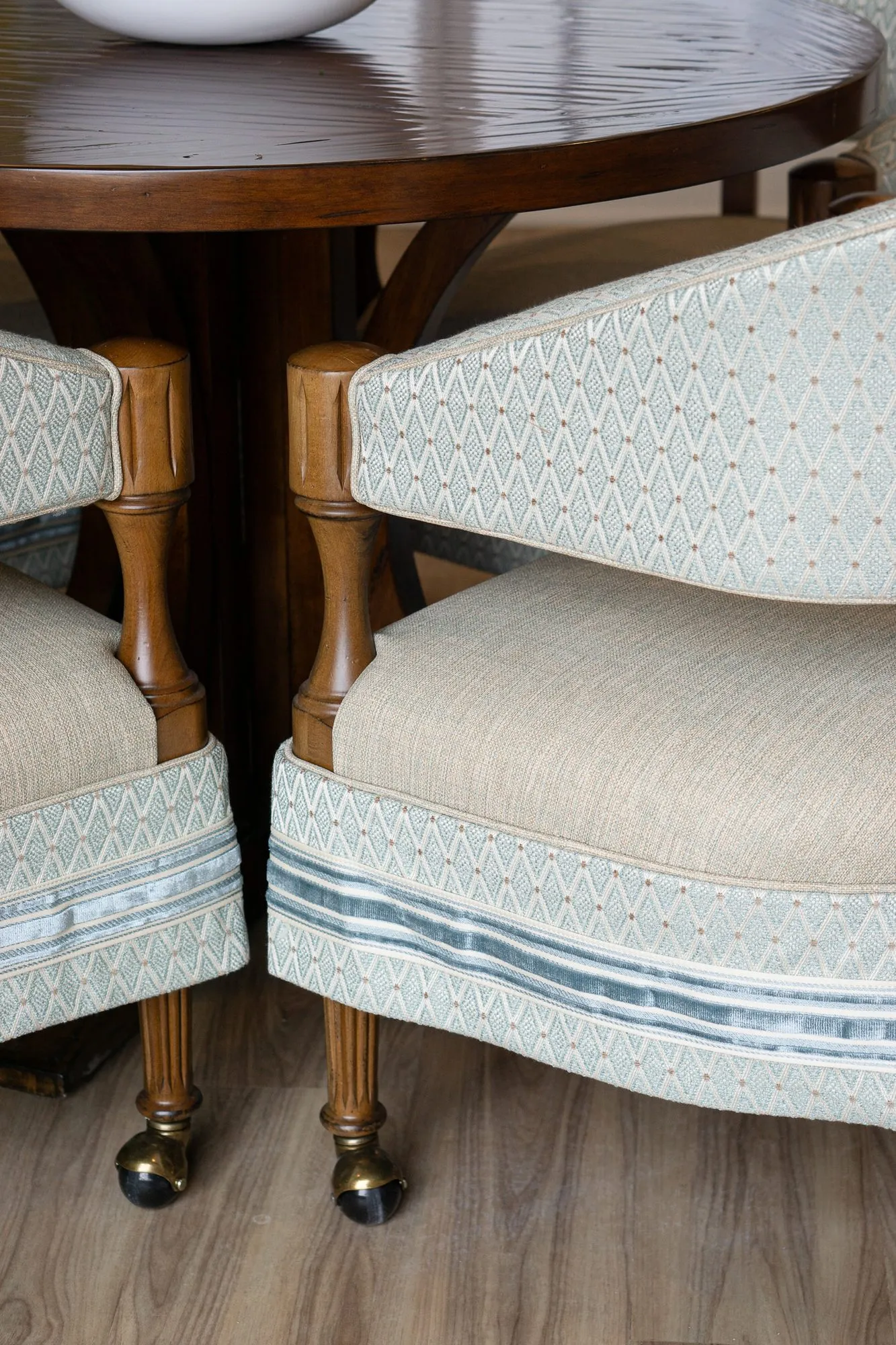 Senior living interior detail: carved wood barrel chairs with pale blue diamond upholstery and striped trim on brass casters