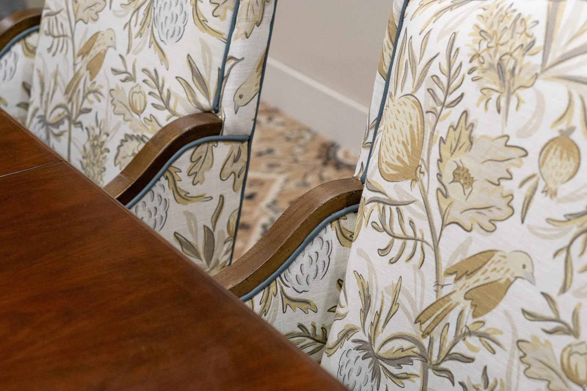 Senior living interior detail: dining chairs upholstered in a bird and botanical print against a walnut table edge