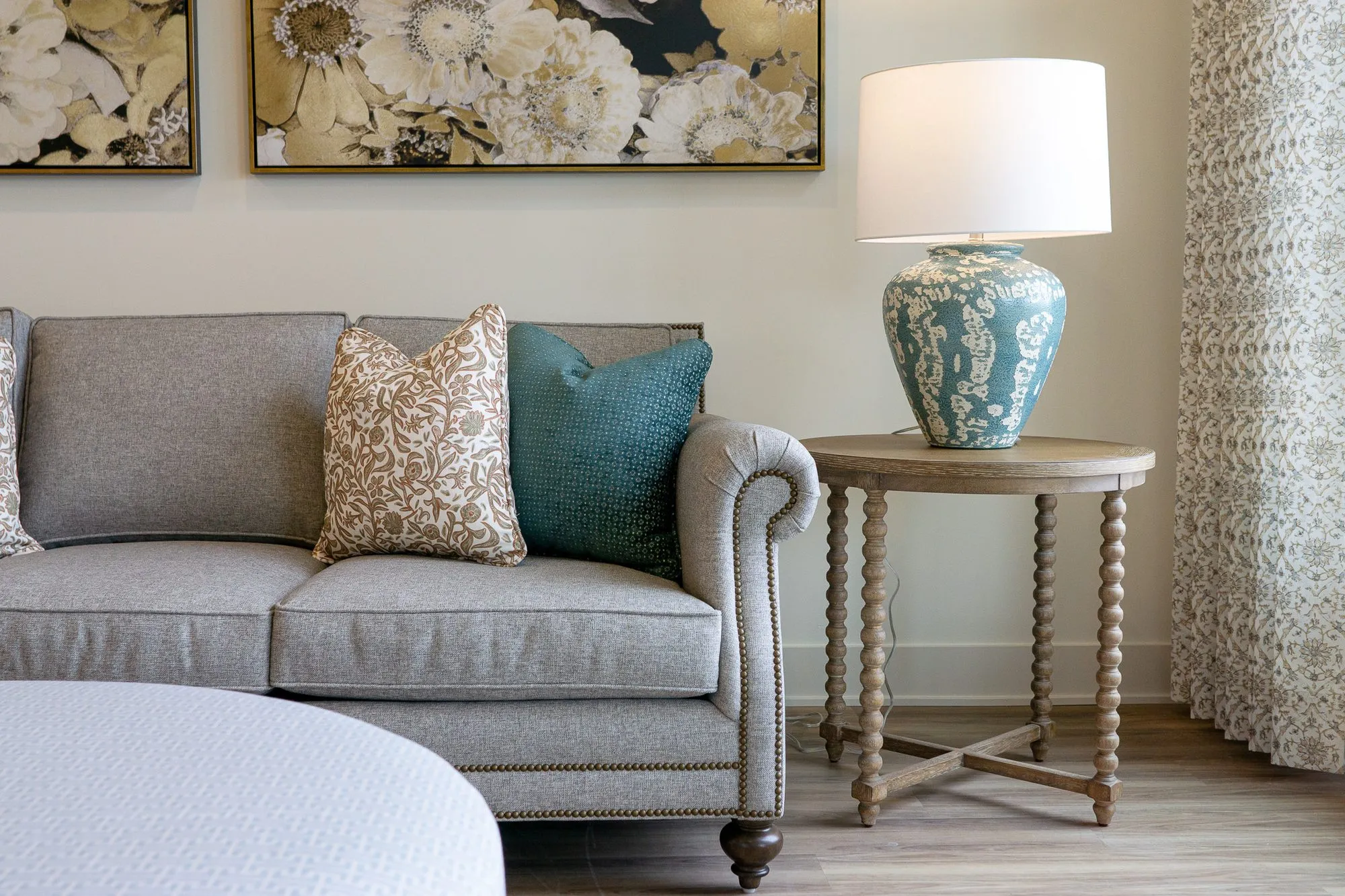 Senior living interior detail: grey rolled-arm sofa with patterned and teal pillows beside a blue lamp on a spindle table