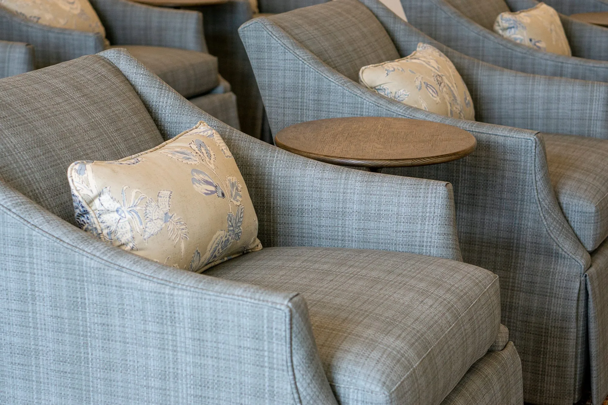 Senior living interior detail: skirted blue plaid armchairs with cream floral pillows around a round drink table