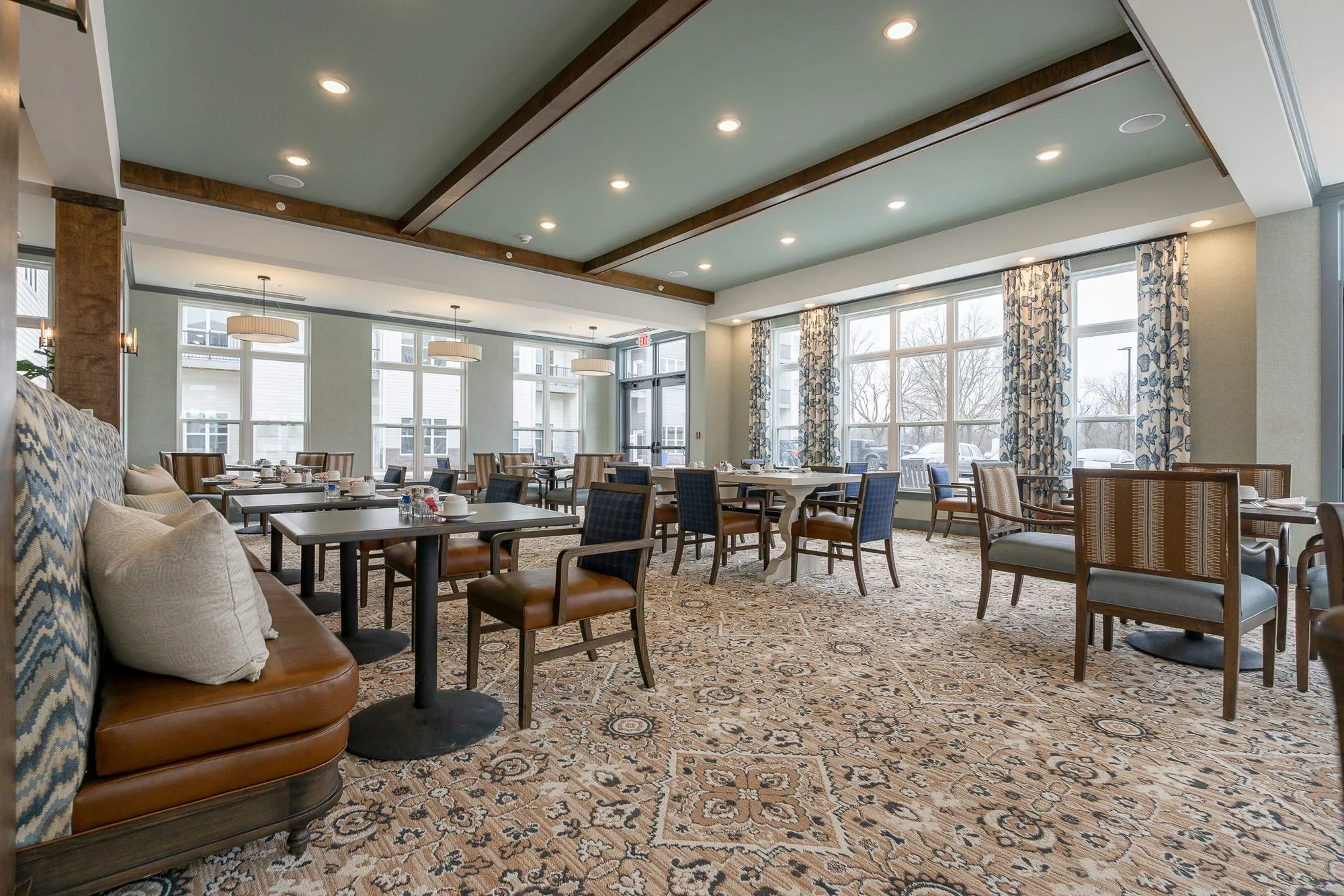 Senior living dining room with a caramel leather banquette and patterned pillows, striped and blue chairs under dark beams