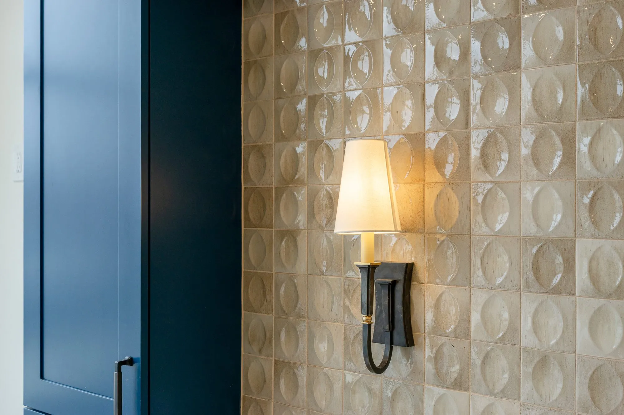 Senior living interior detail: landscape close-up of the bronze sconce on glossy lens pattern tile by navy cabinetry