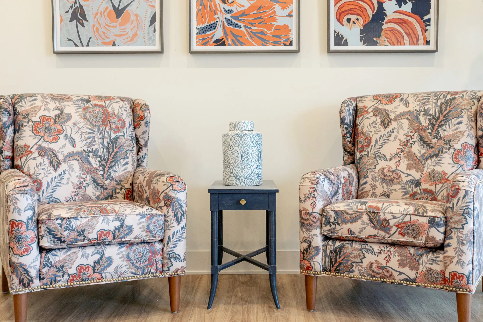 Senior living interior detail: pair of floral wing chairs either side of a navy side table, three floral prints above