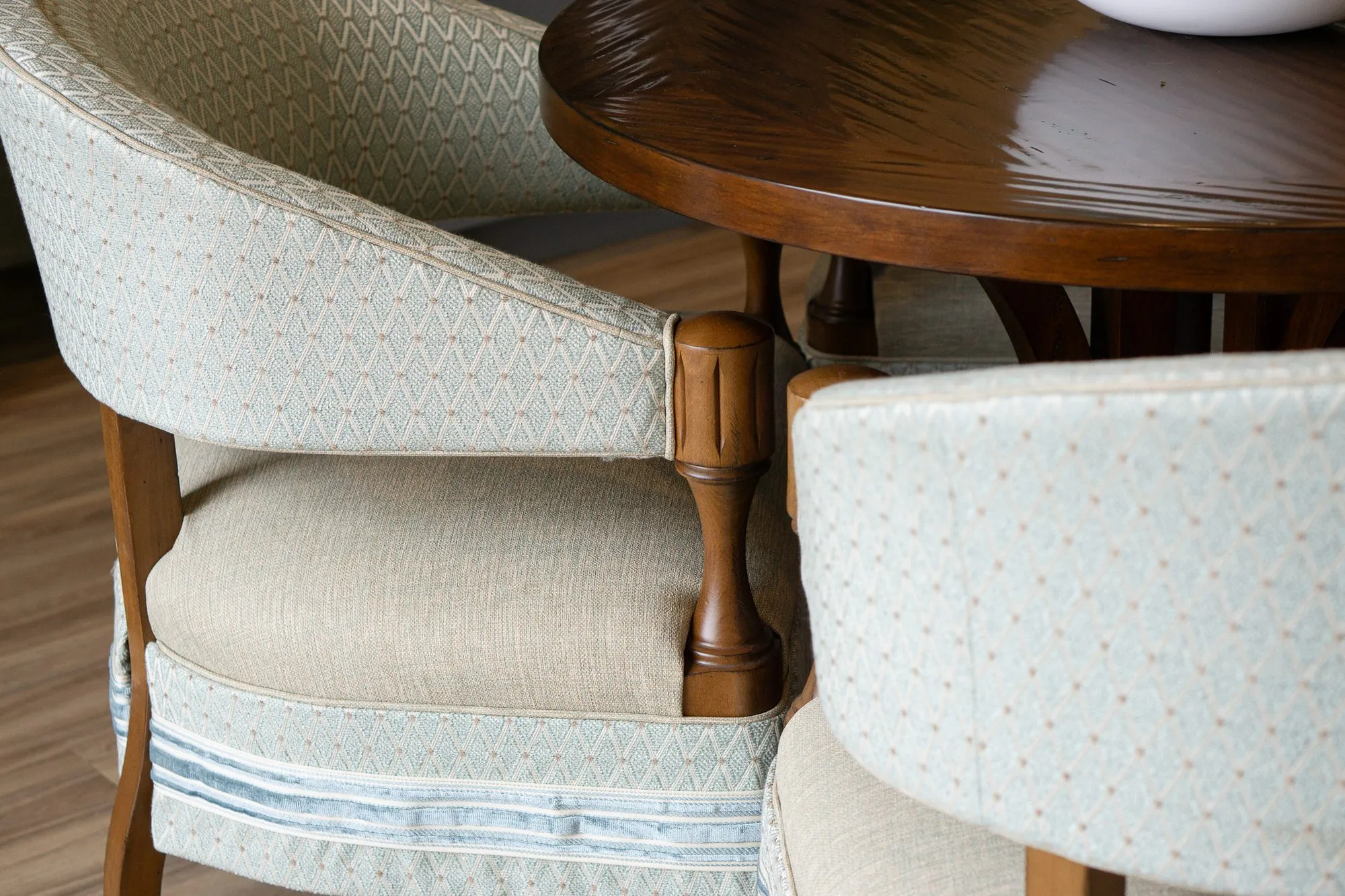 Senior living interior detail: pale blue diamond upholstered barrel chairs with turned wood arms at a round walnut table