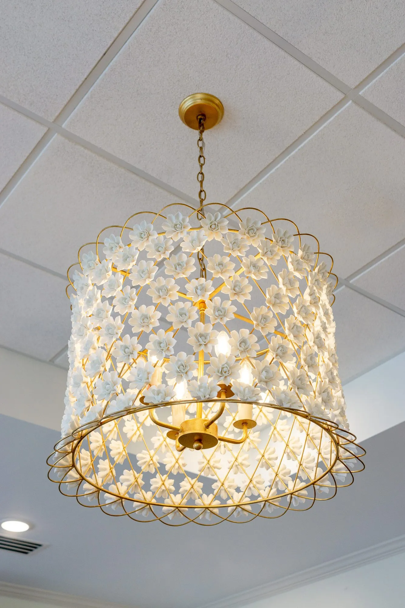 Senior living interior detail: gold chandelier covered in white porcelain flowers hung from a ceiling grid