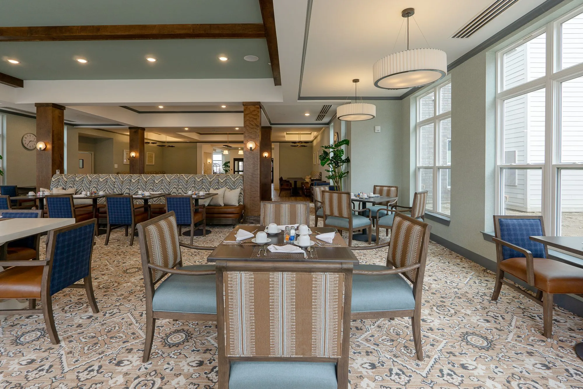 Senior living dining room with striped and blue chairs at a set table, a chevron banquette and timber columns beyond