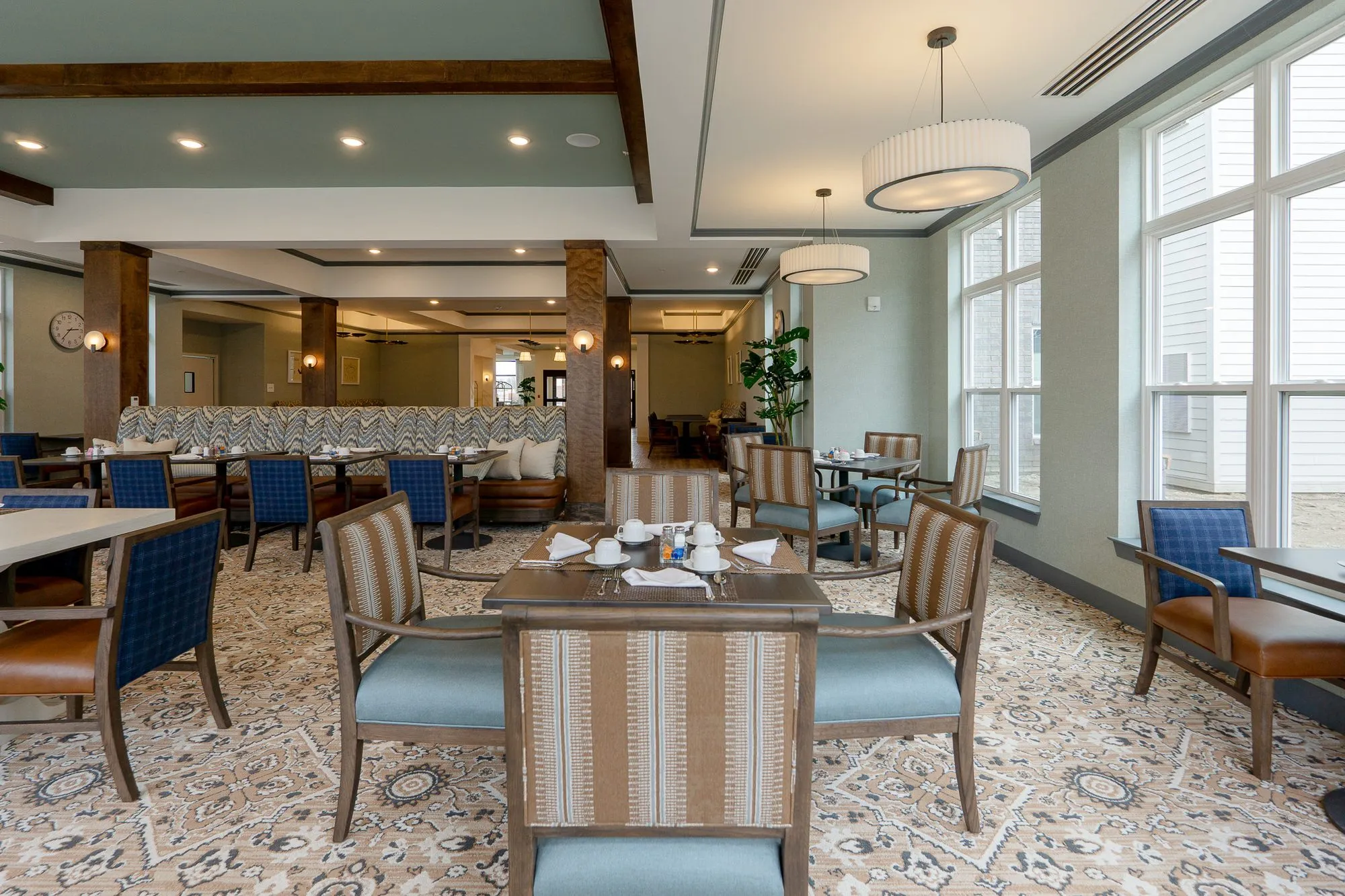 Senior living dining room with a striped chair at a set table, the chevron banquette and timber columns under drum pendants