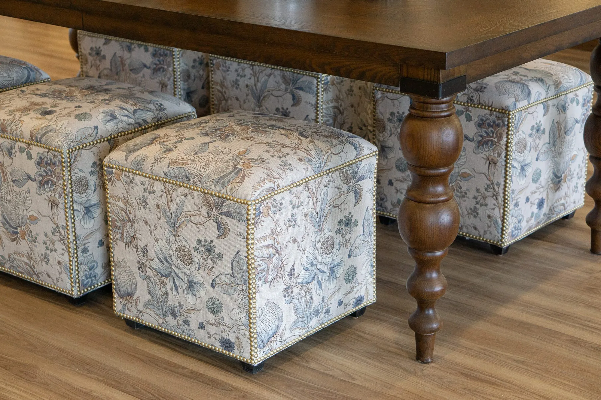 Senior living interior detail: blue and cream floral cube ottomans with nailhead trim beside a turned walnut table leg