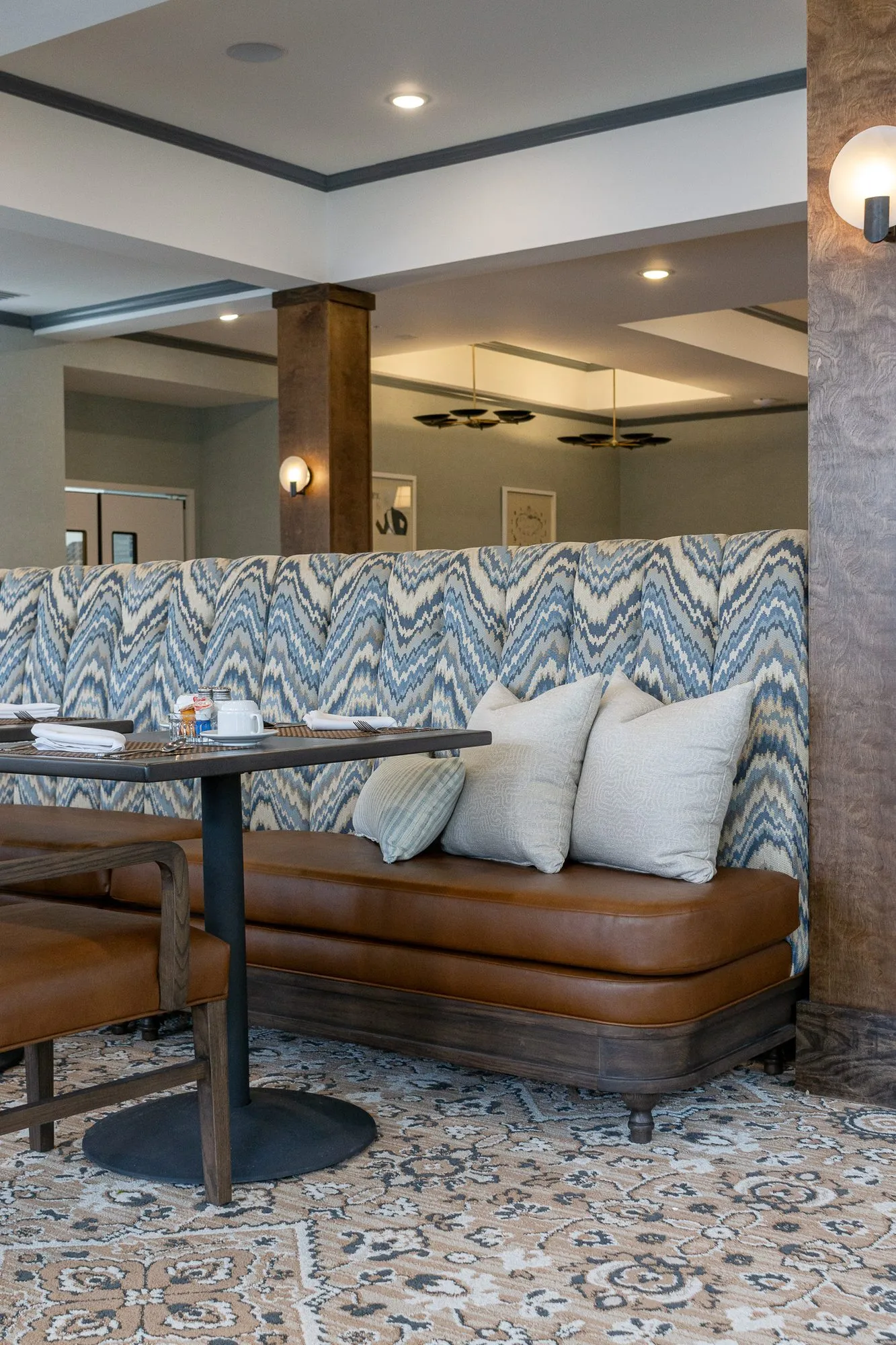 Senior living interior detail: chevron upholstered banquette with tan leather seat and cream pillows beside a timber column