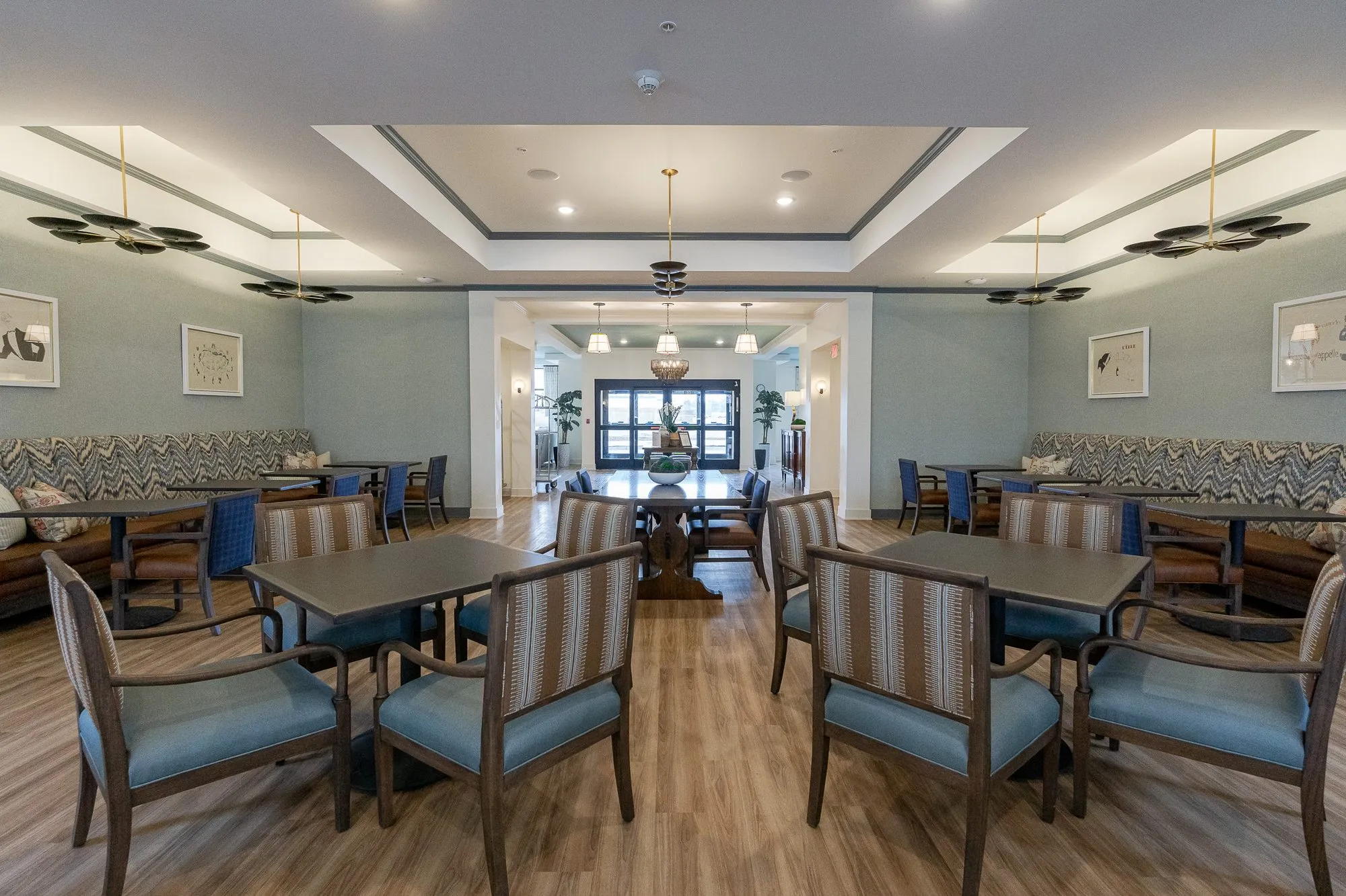 Senior living bistro with striped chairs around tables, chevron banquettes along both walls under black disc pendants