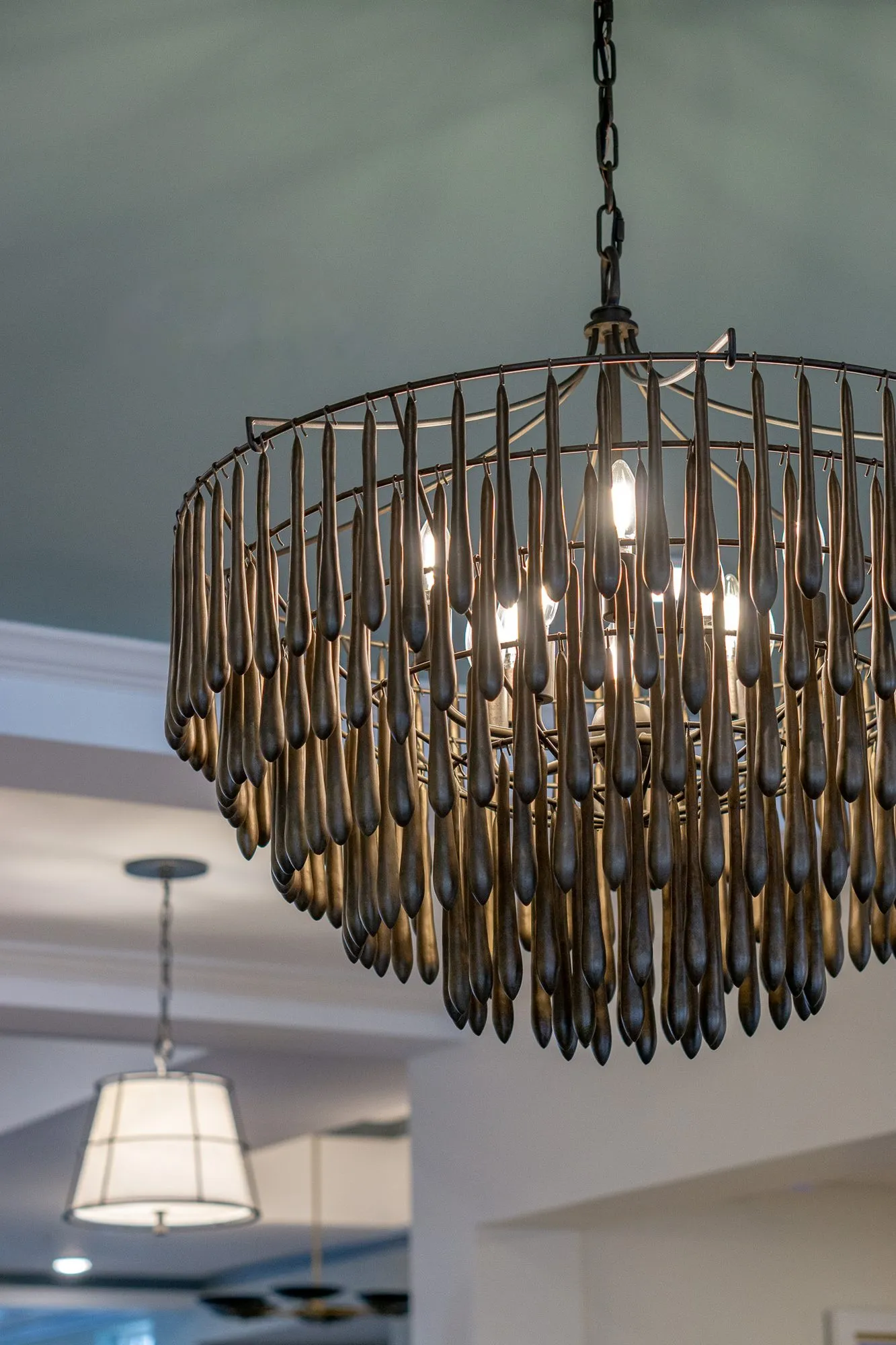 Senior living interior detail: wood bead chandelier hanging from an aqua ceiling, a drum pendant beyond