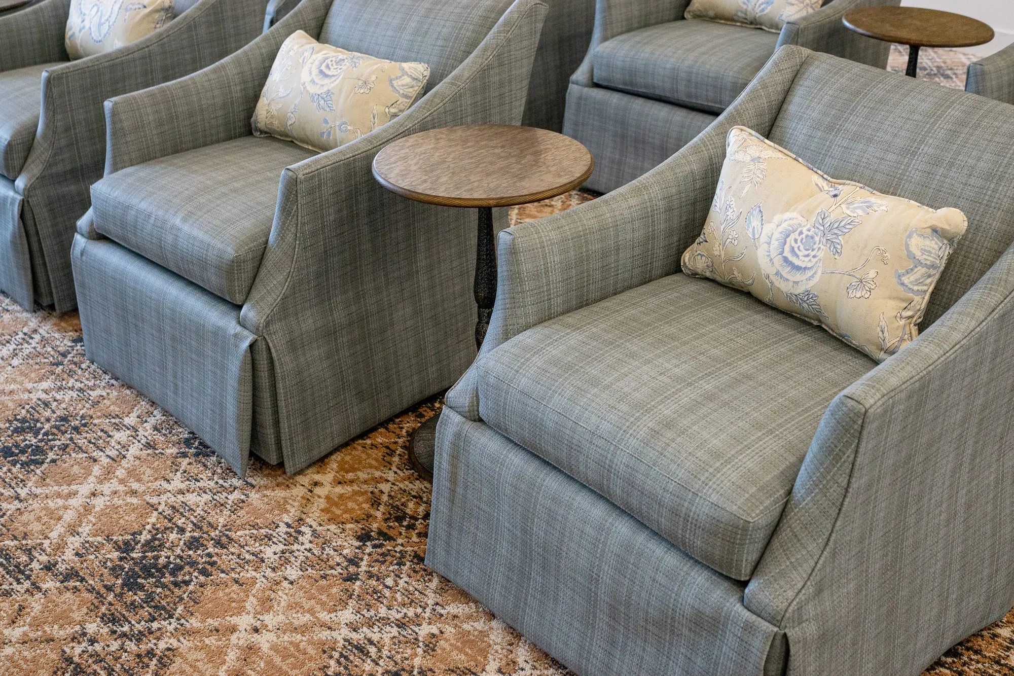 Senior living interior detail: overhead view of skirted plaid armchairs with floral pillows and drink tables on plaid carpet