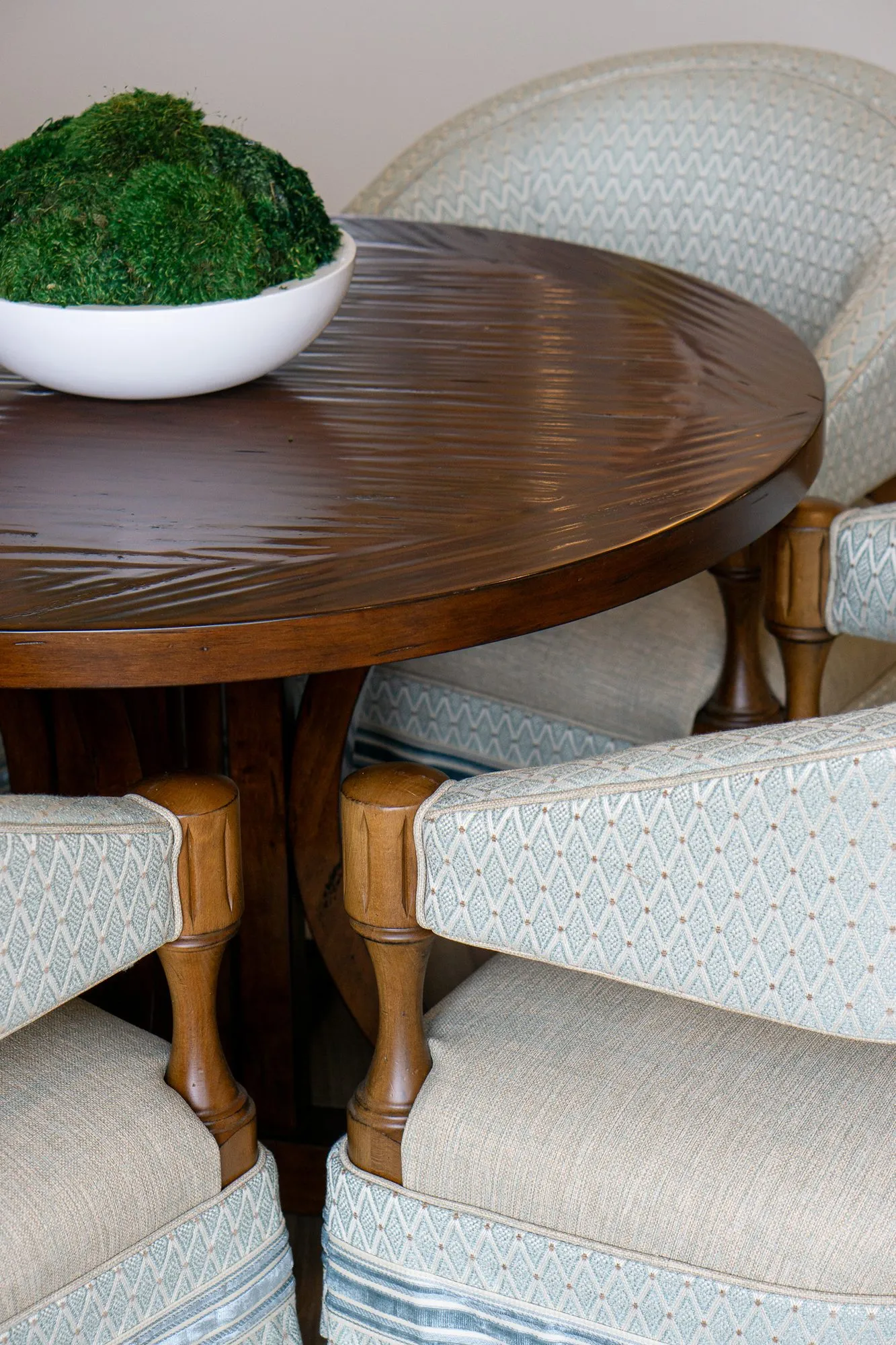 Senior living interior detail: moss bowl on a round walnut table among pale blue diamond upholstered barrel chairs