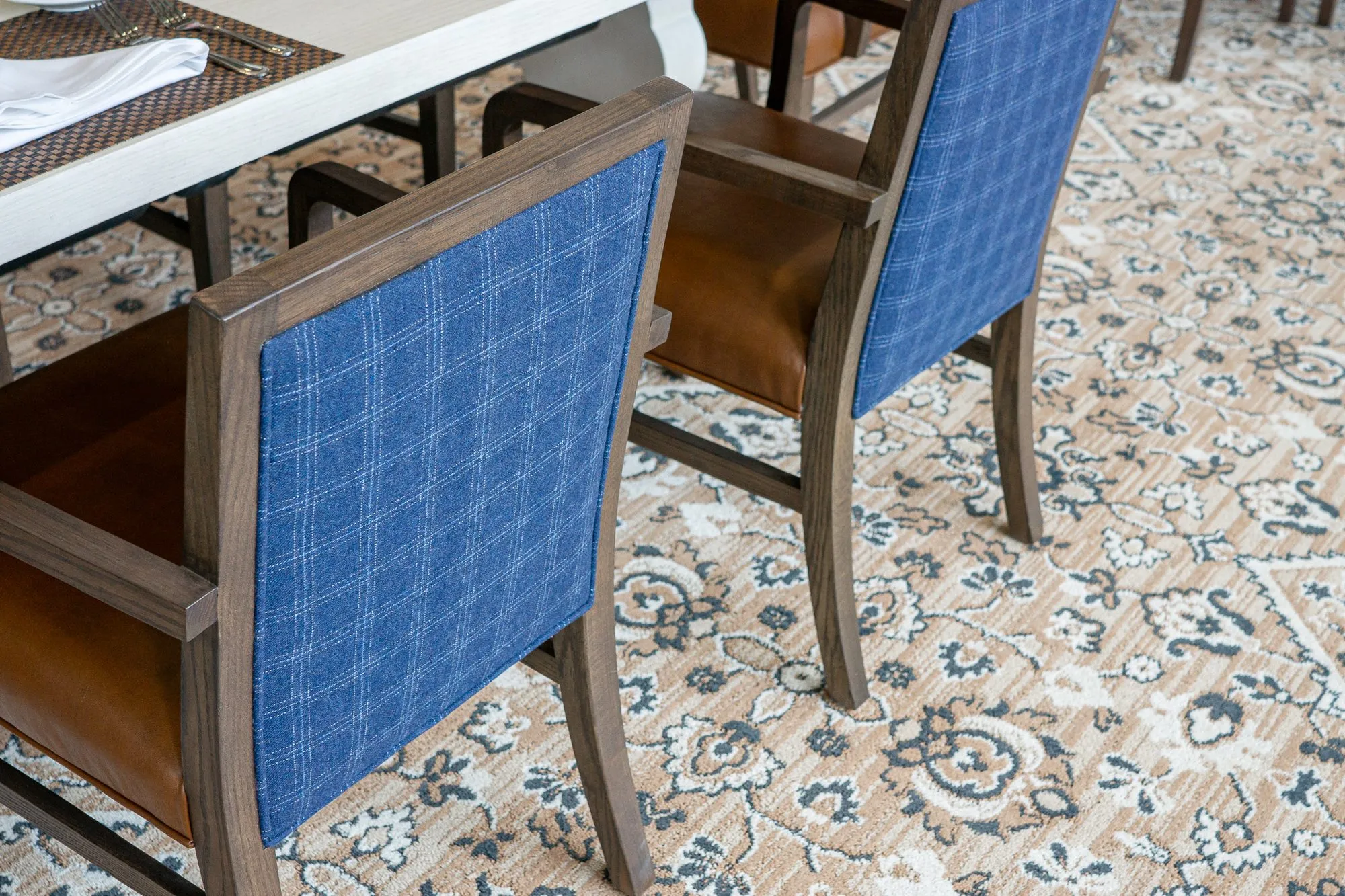Senior living interior detail: blue plaid chair backs at a dining table on patterned carpet