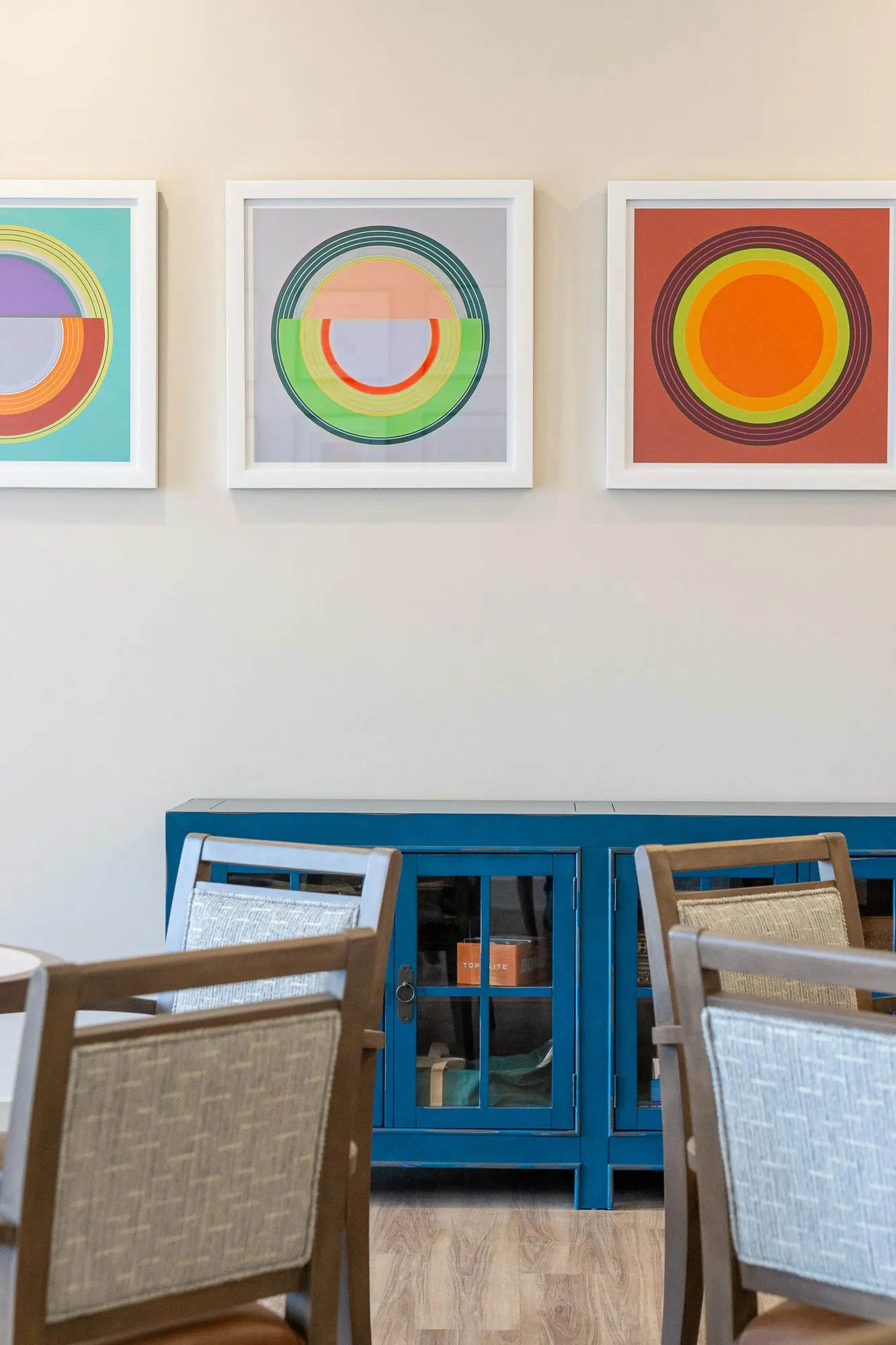 Senior living interior detail: circle prints above a blue cabinet, grey wood chair backs in the foreground