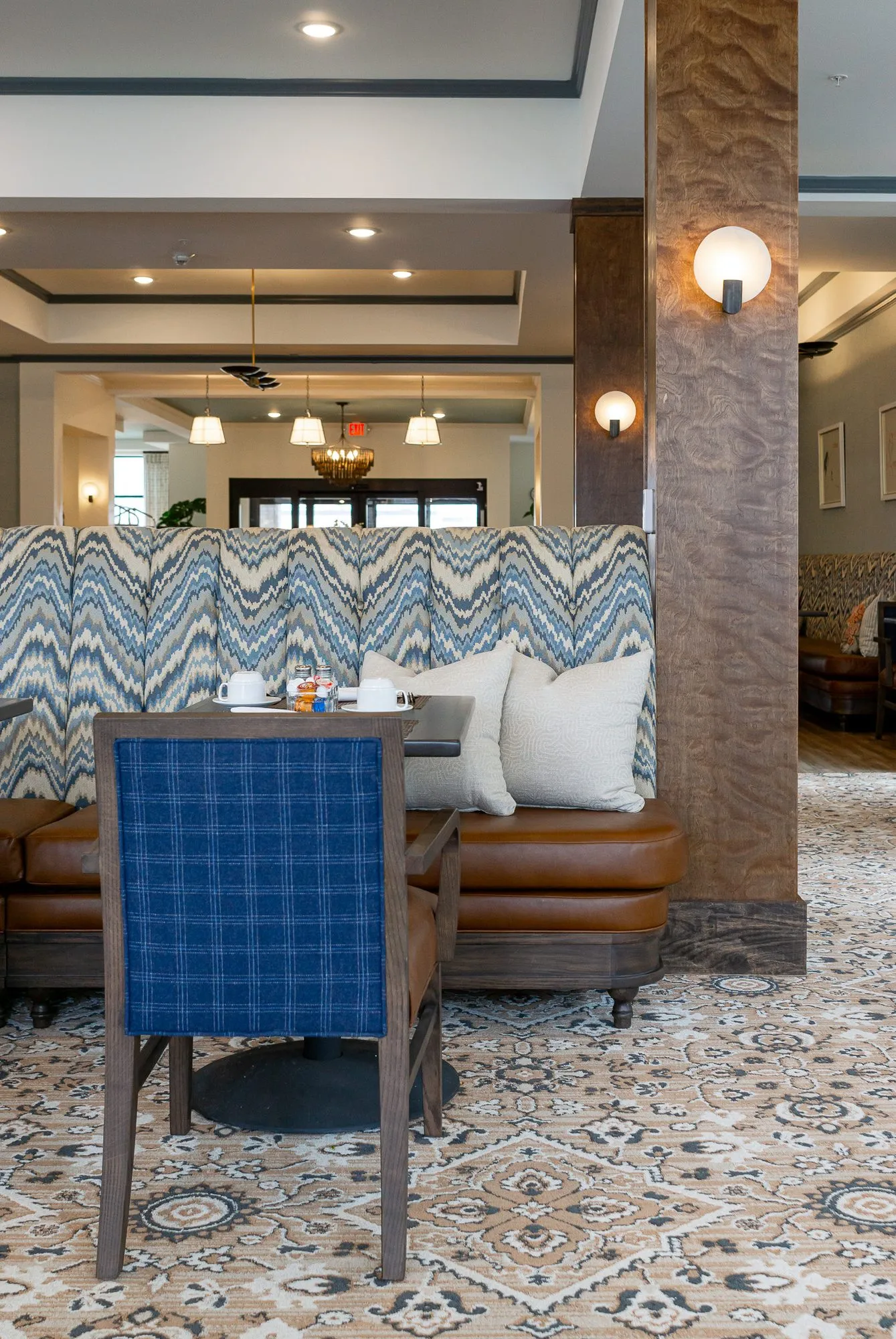 Senior living dining room, a blue plaid chair at a table before the chevron banquette and a timber column with sconces