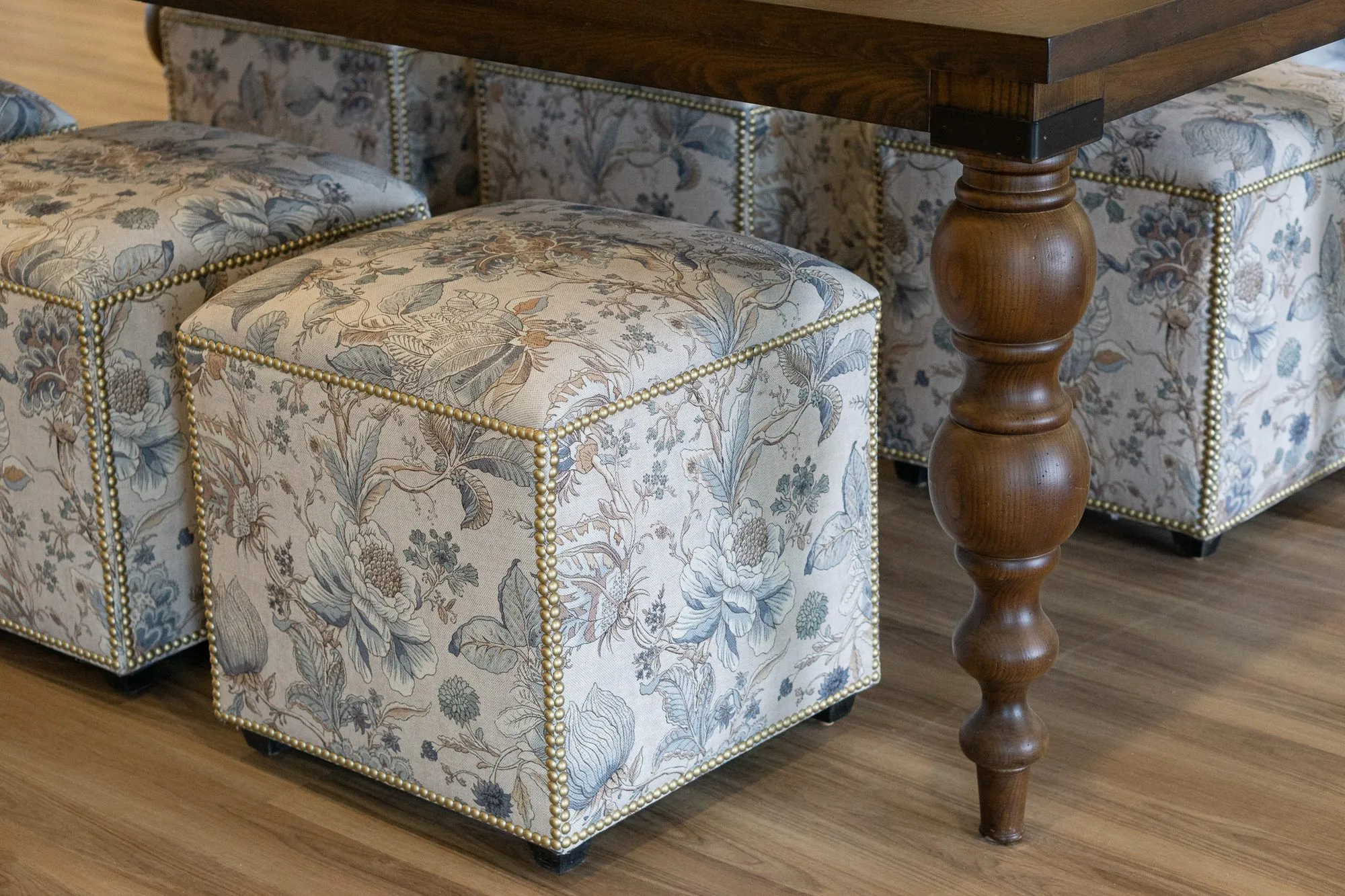 Senior living interior detail: blue and cream floral cube ottomans with nailhead trim tucked under a walnut table