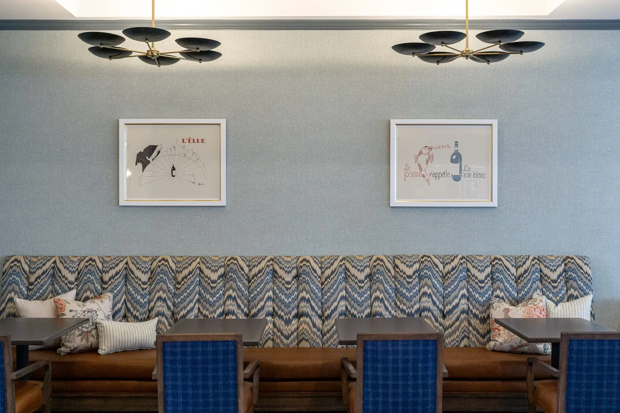 Senior living dining room with a chevron banquette below two framed prints and black disc chandeliers on a blue wall