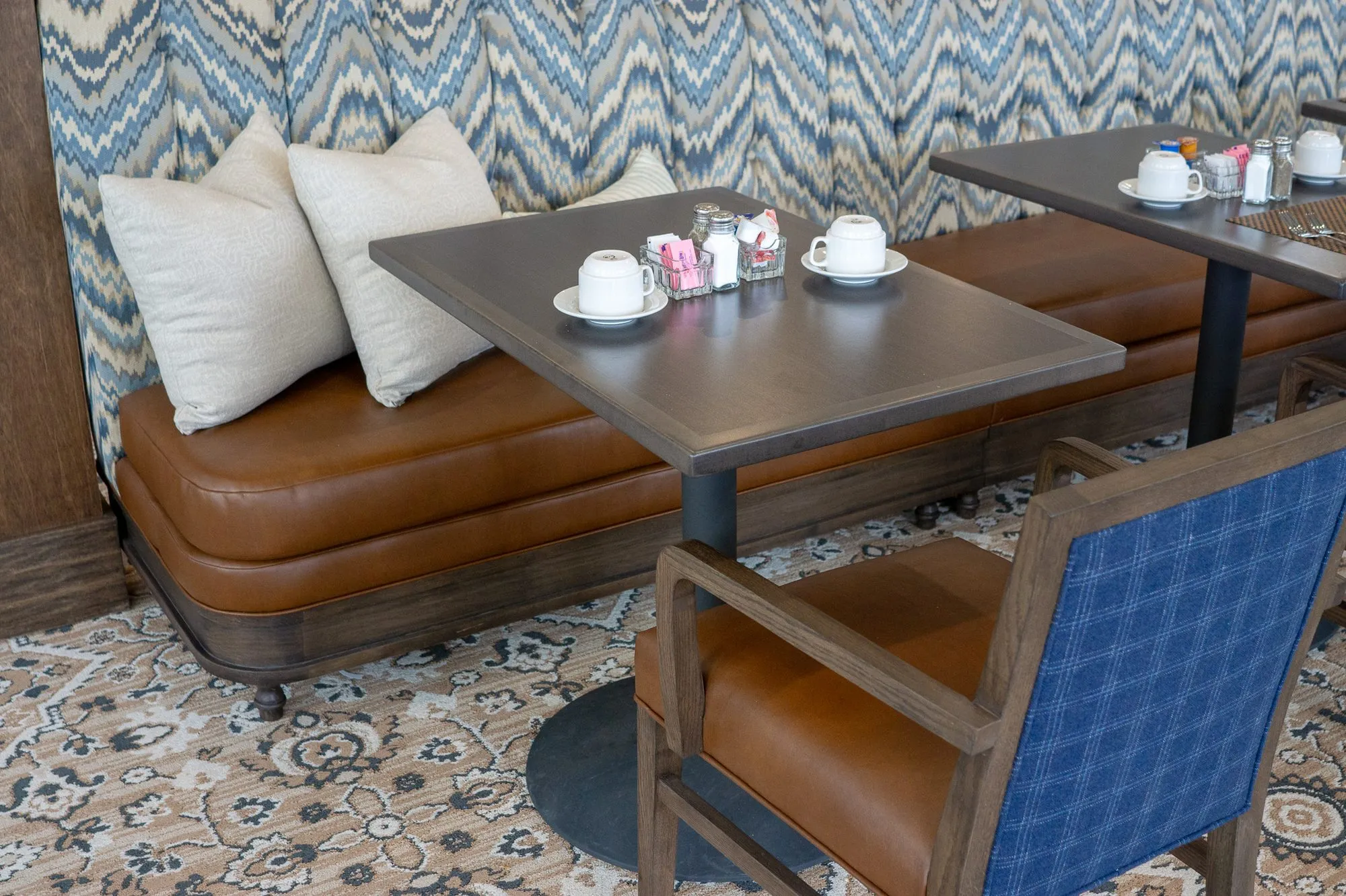 Senior living interior detail: set table with cups at the tan leather banquette, a blue plaid chair in front