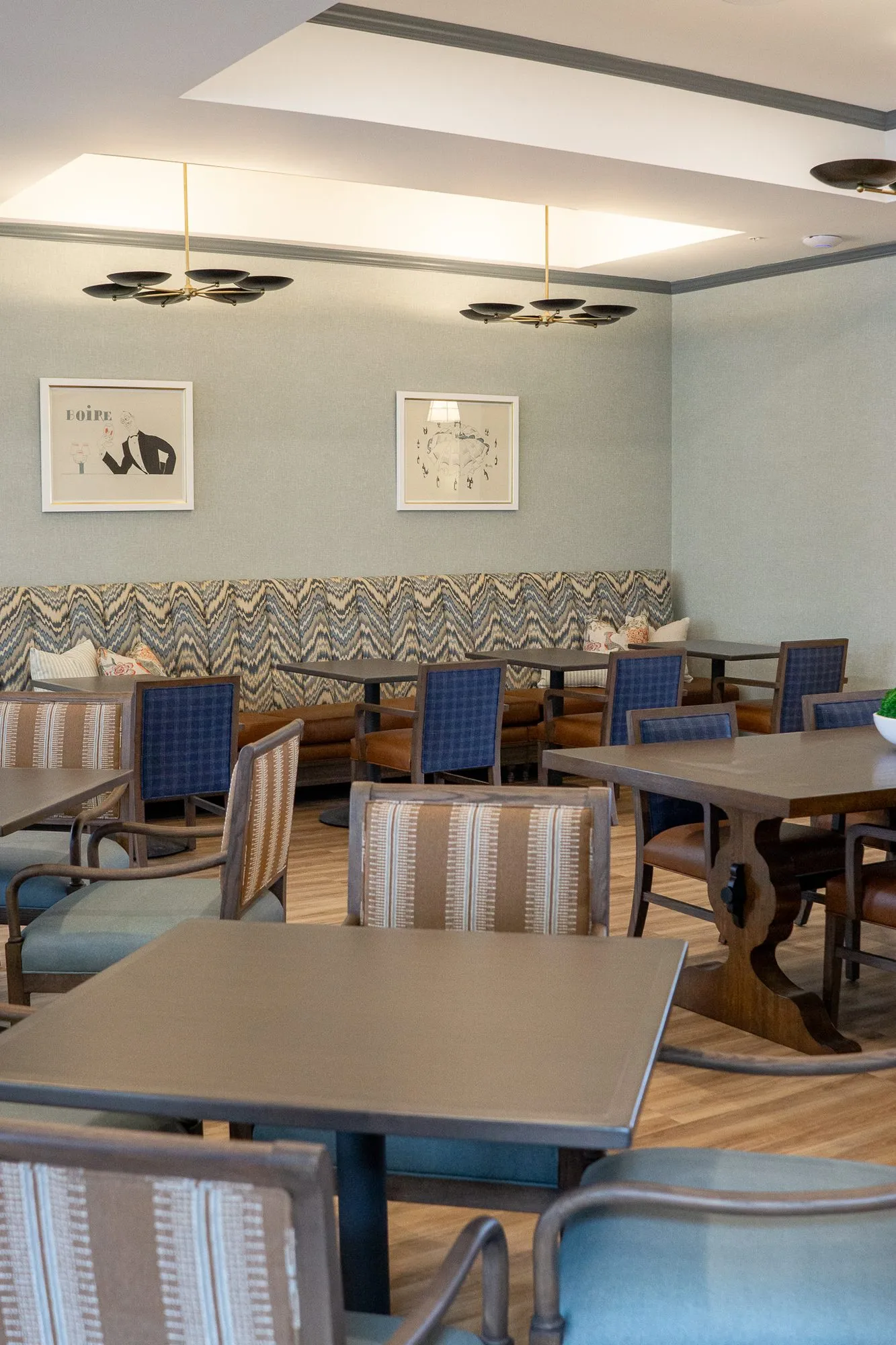 Senior living bistro with striped chairs in front and blue plaid chairs at the chevron banquette under disc pendants
