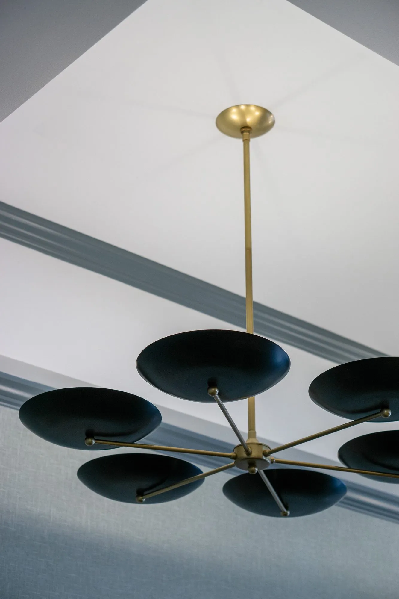 Senior living interior detail: looking up at a brass chandelier with black saucer shades below a white tray ceiling