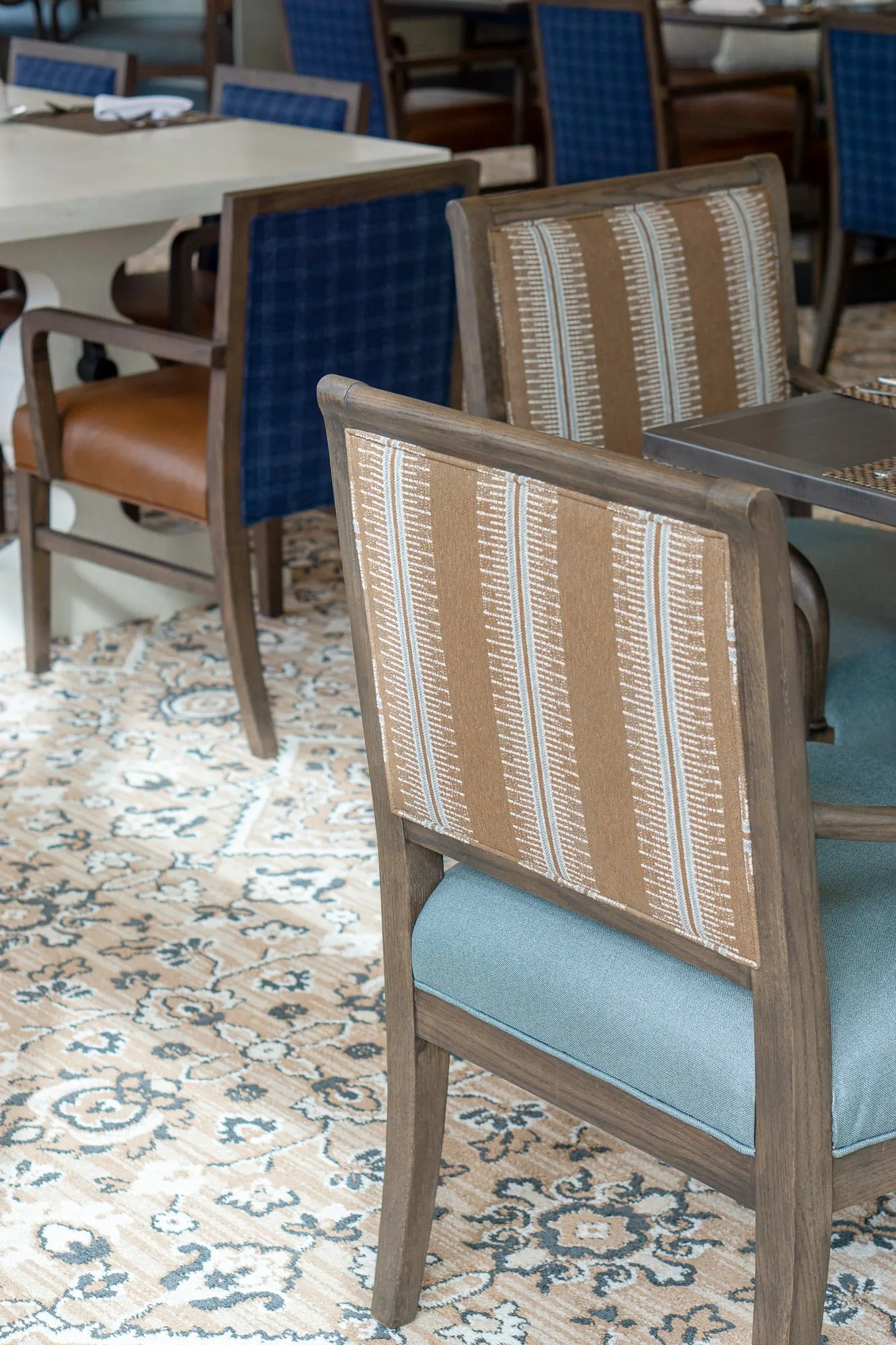 Senior living interior detail: striped tan and white chair backs with blue seats, blue plaid chairs at a table beyond