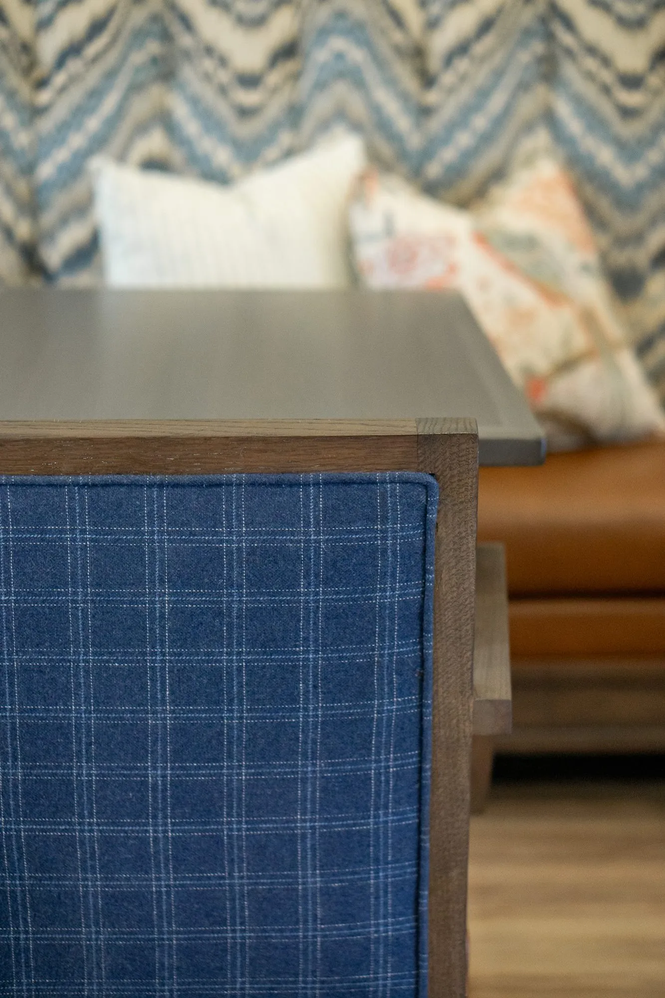 Senior living interior detail: blue plaid chair back at a table, the chevron banquette and pillows softly behind
