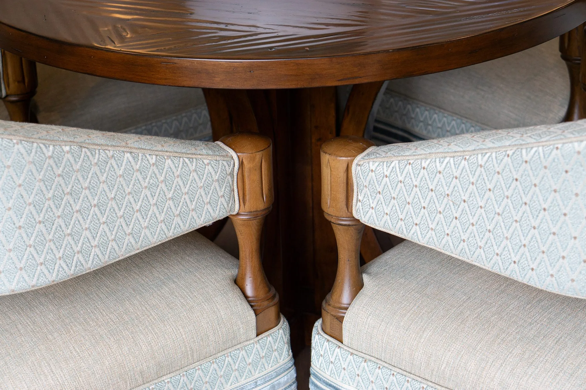Senior living interior detail: turned wood arms of two pale blue barrel chairs meeting at a walnut table base