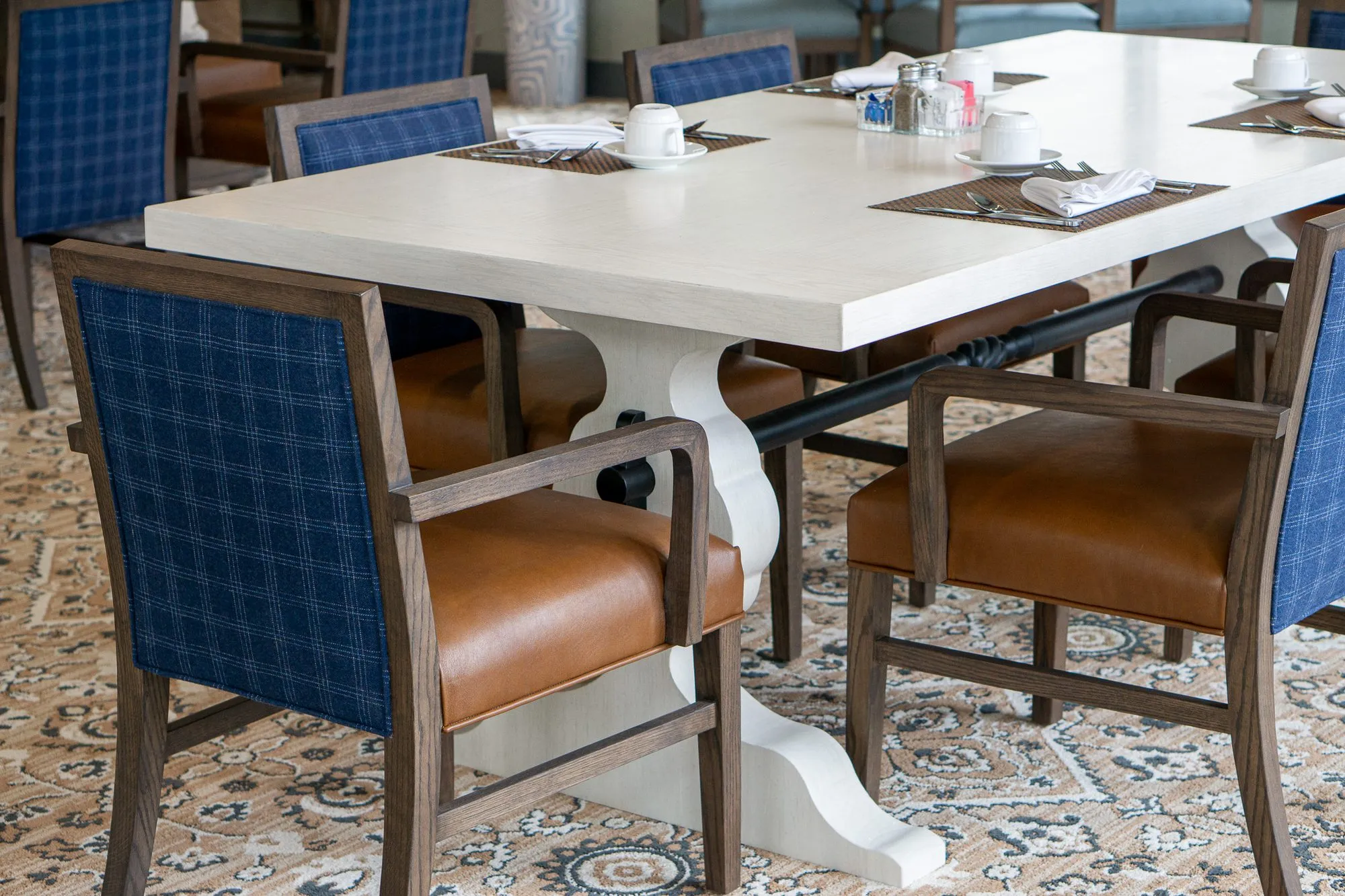 Senior living dining room with blue plaid chairs with tan leather seats around a white trestle table set with cups