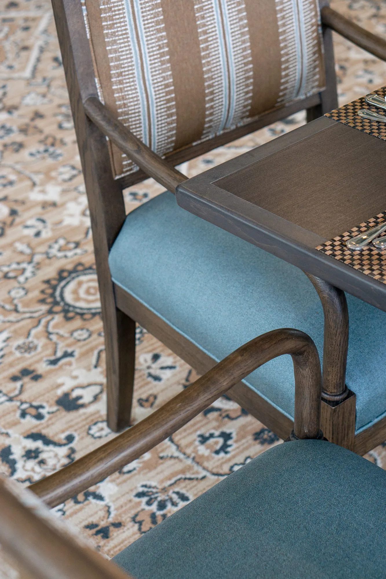 Senior living interior detail: overhead view of a striped chair with a blue seat at a table on the medallion carpet