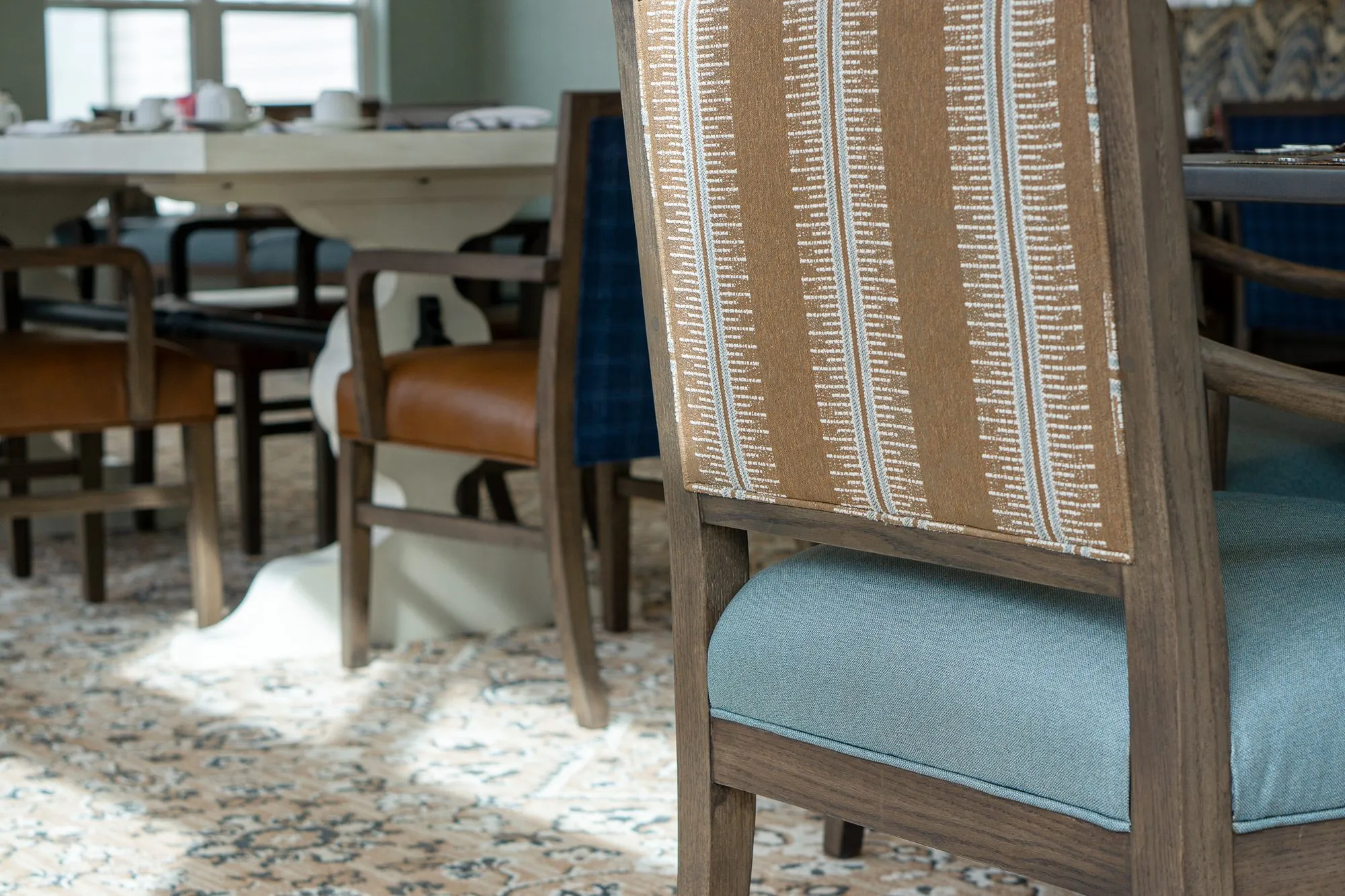 Senior living interior detail: striped chair back with a blue seat, blue plaid chairs at a white table beyond