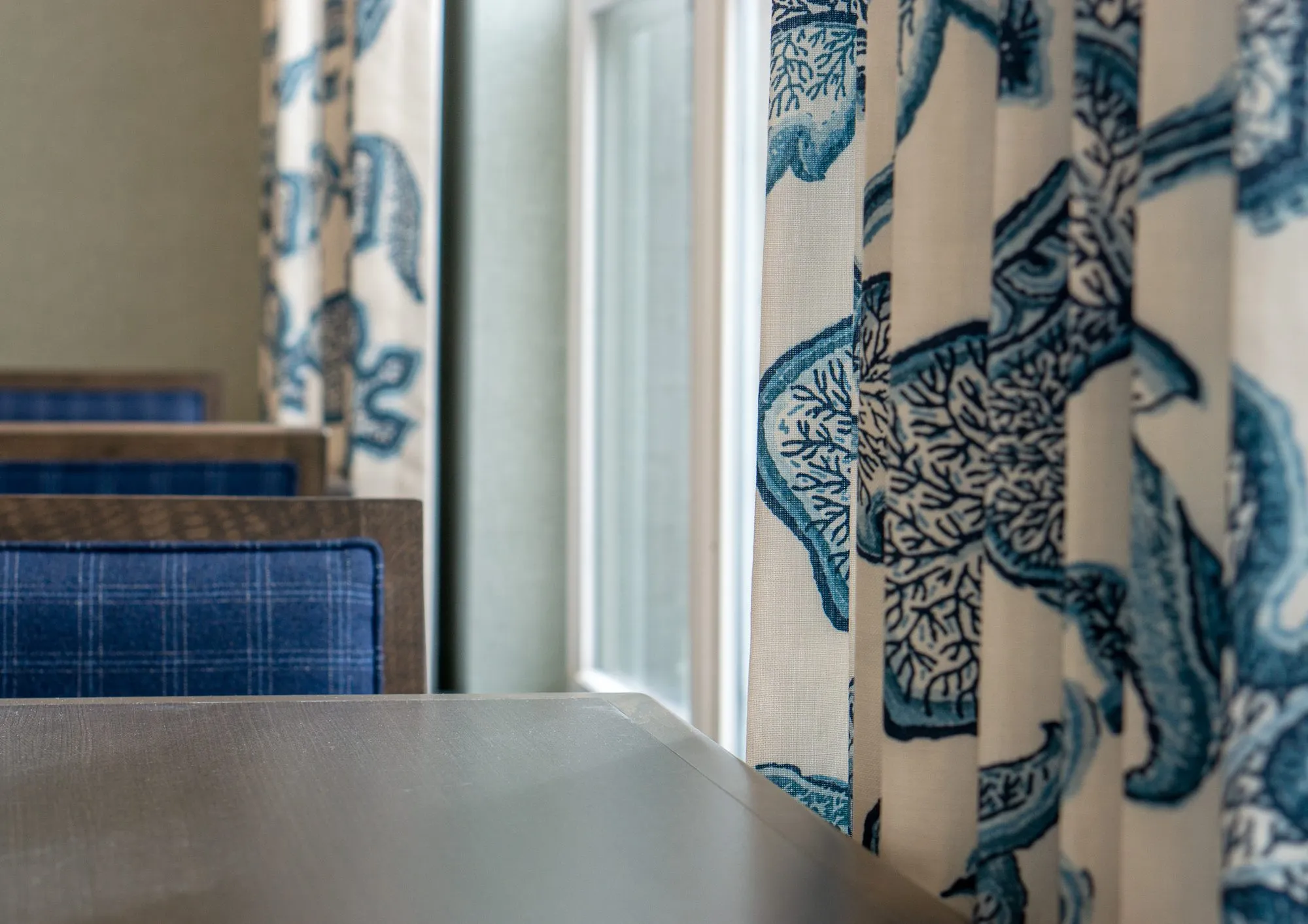 Senior living interior detail: blue and white botanical print curtains by a window, blue plaid chairs at a table