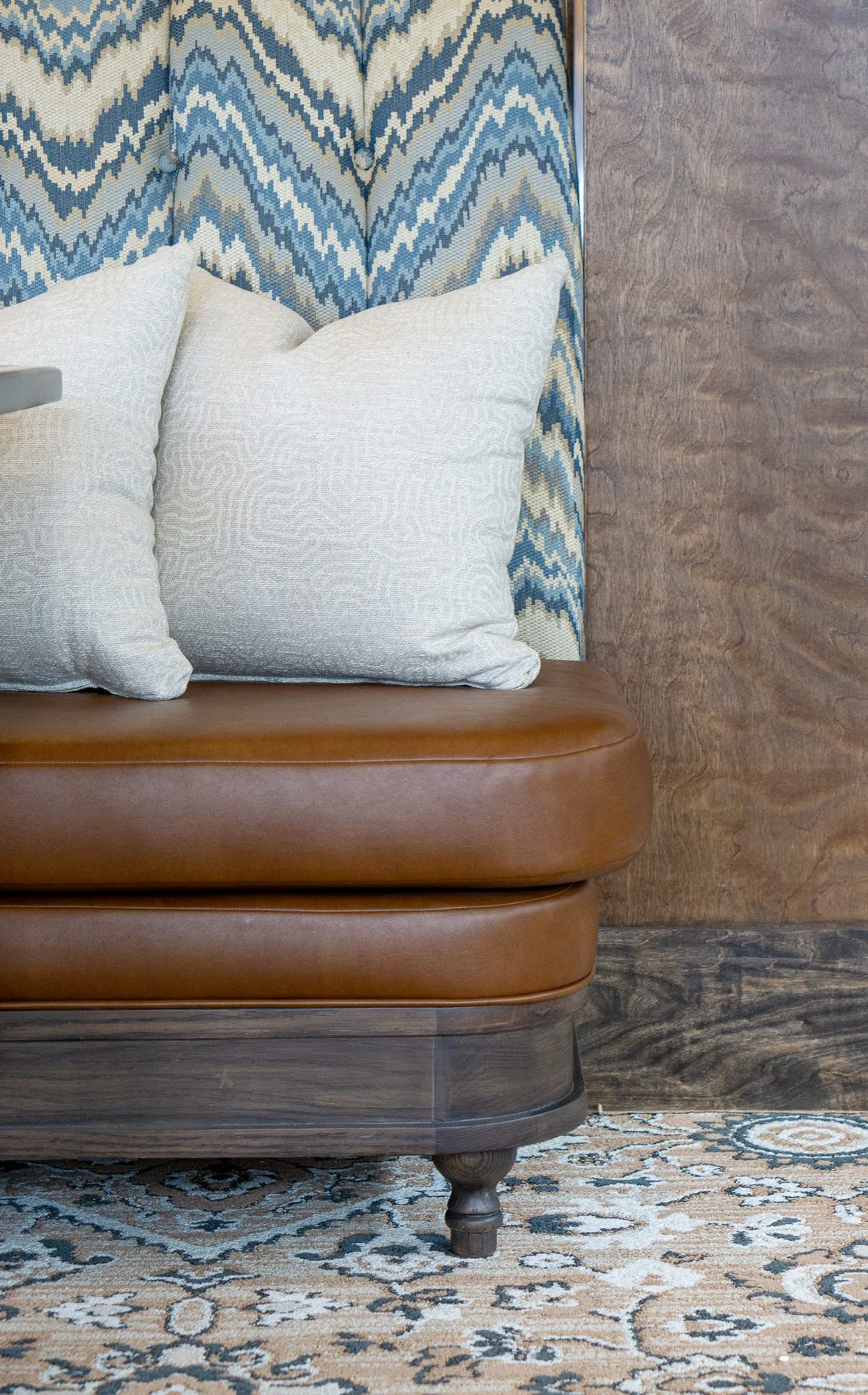 Senior living interior detail: tan leather banquette on turned feet with cream pillows against the chevron back