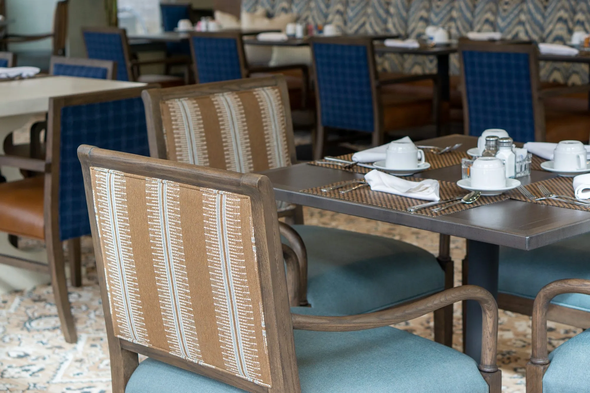 Senior living dining room with striped blue-seated chairs at a set table, blue plaid chairs and the chevron banquette behind
