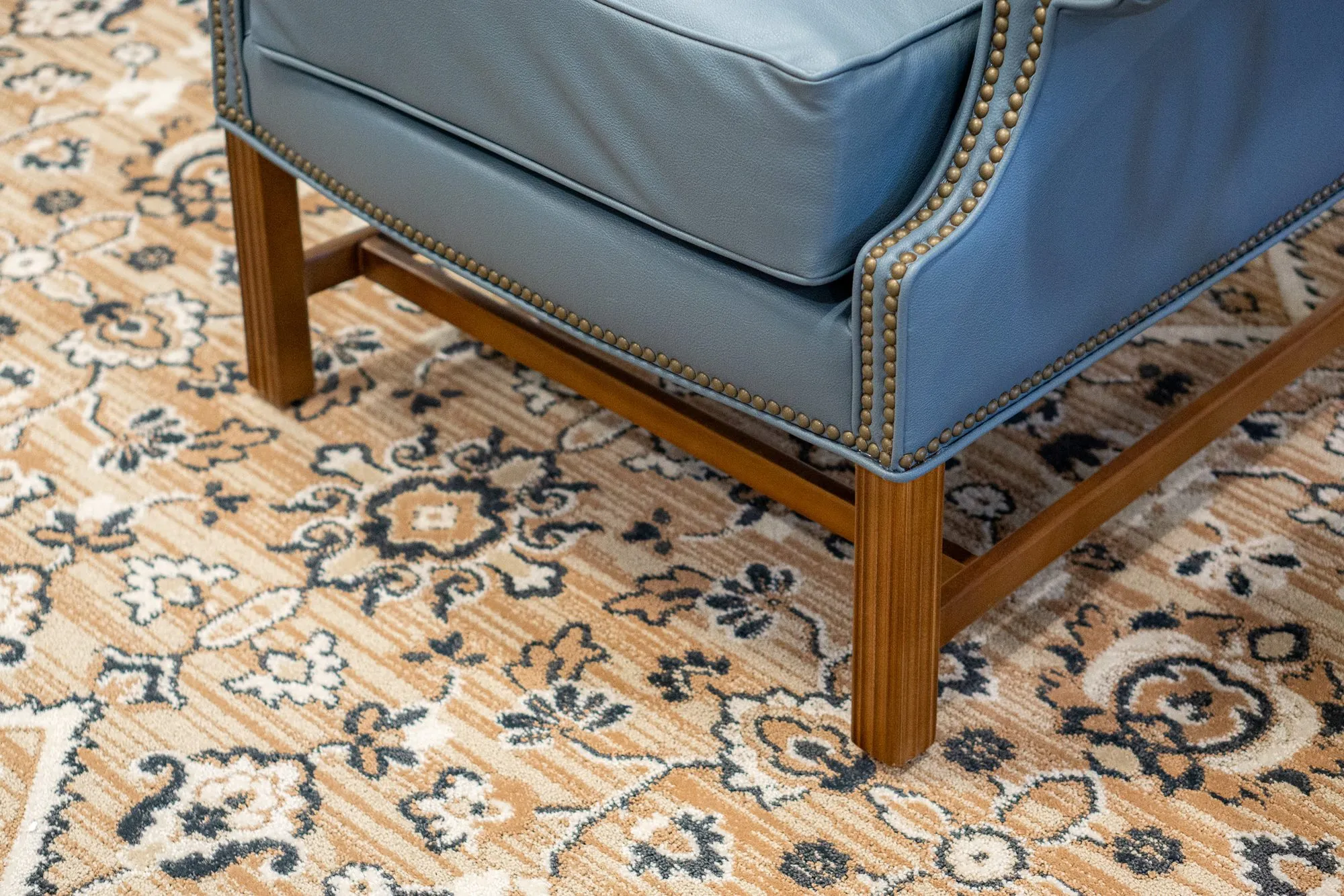 Senior living interior detail: blue leather wing chair's nailhead trim and wood legs on a patterned rug