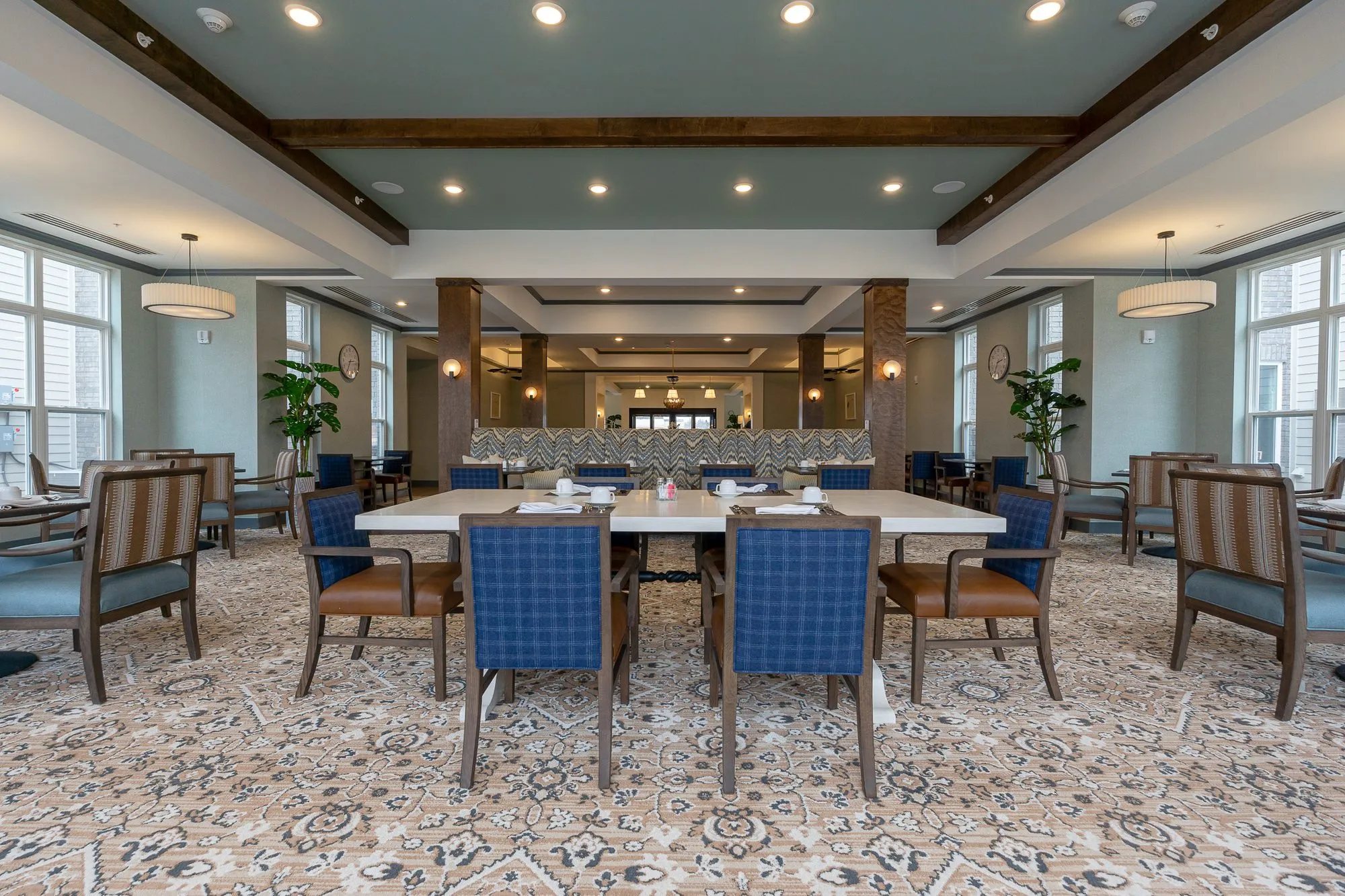 Senior living dining room, centred on blue plaid chairs around a white table before the chevron banquette and columns