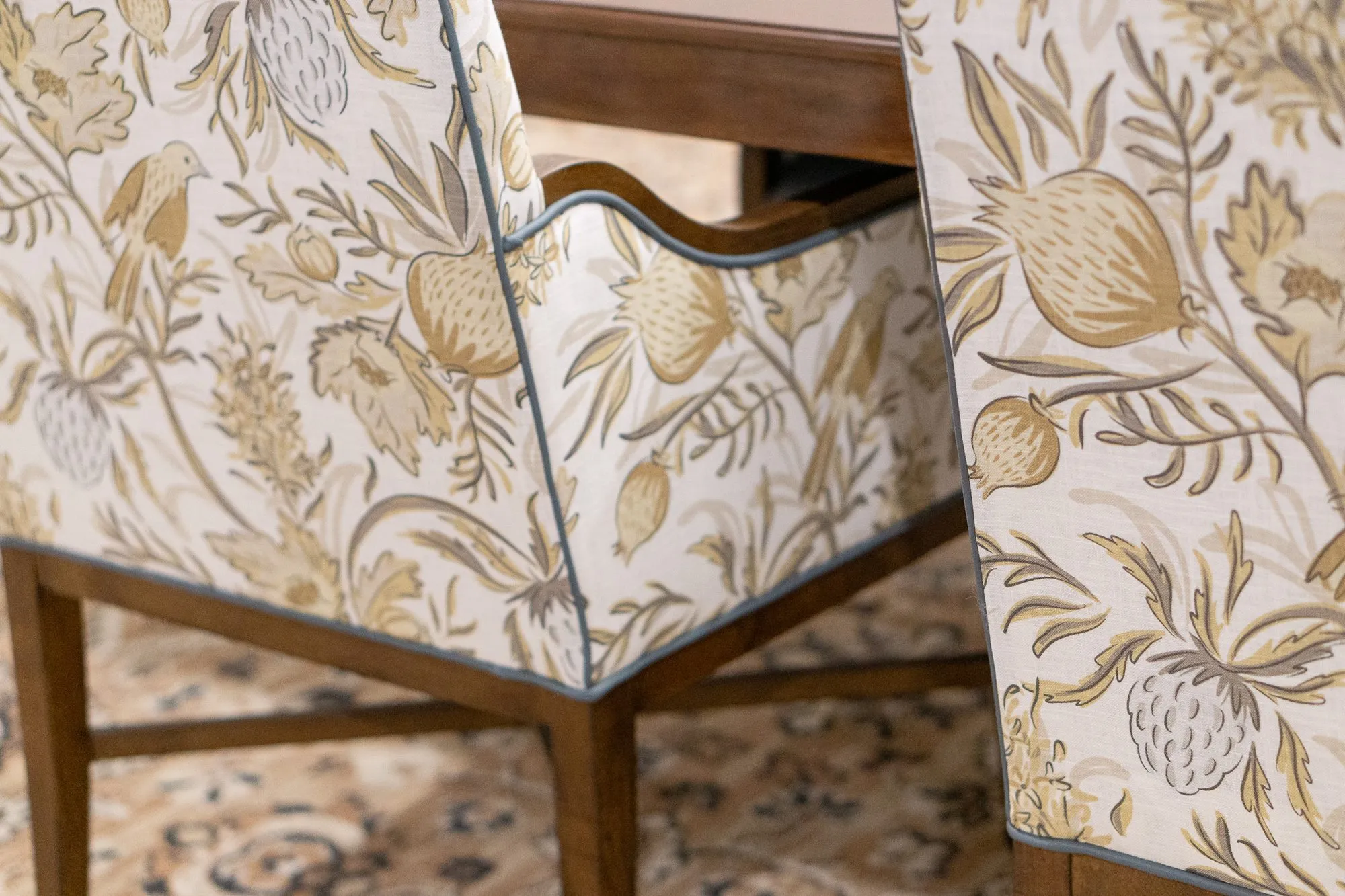 Senior living interior detail: bird and botanical print dining chairs with piped edges beside a walnut table