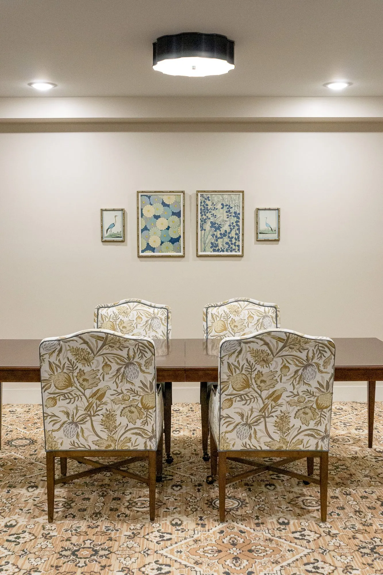 Senior living private dining table with botanical print chairs below four framed botanical prints and a black drum light