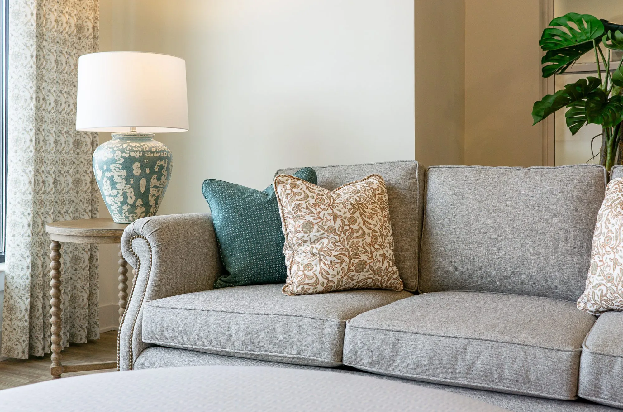 Senior living interior detail: grey rolled-arm sofa with teal and patterned pillows beside a blue lamp on a spindle table