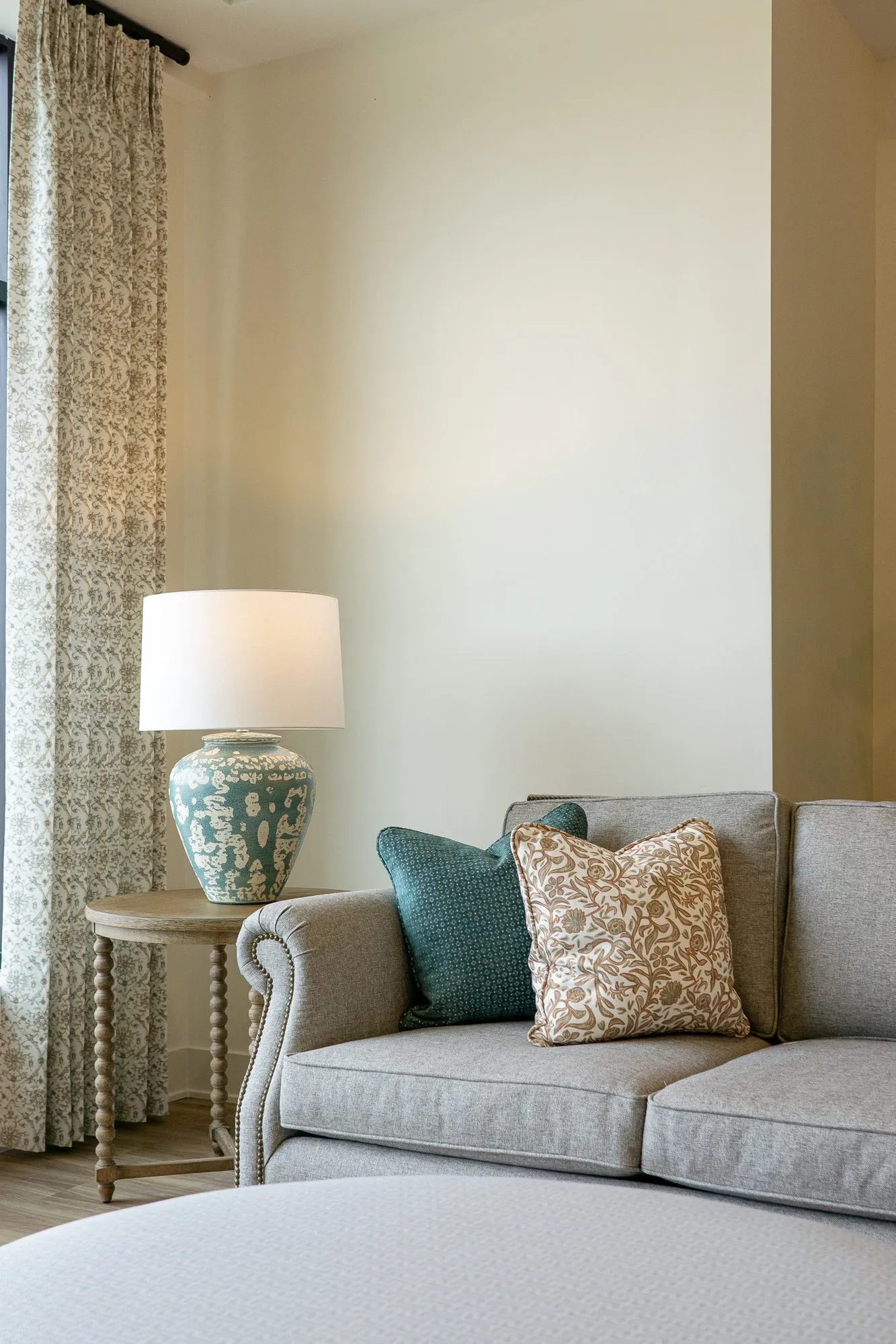 Senior living interior detail: grey sofa with pillows below a blue ceramic lamp by patterned curtains