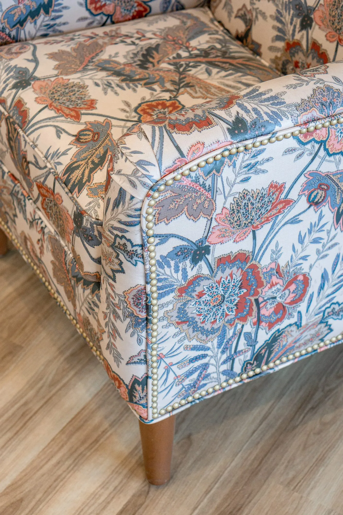 Senior living interior detail: overhead view of a floral print wing chair with nailhead trim on a wood floor