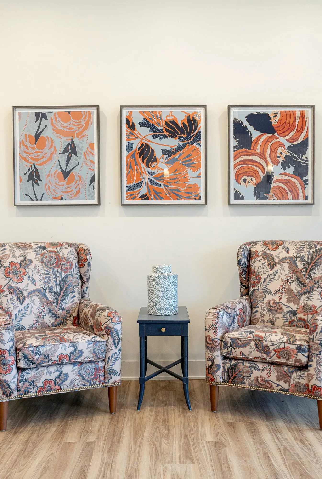 Senior living interior detail: two floral wing chairs either side of a navy side table under three botanical prints