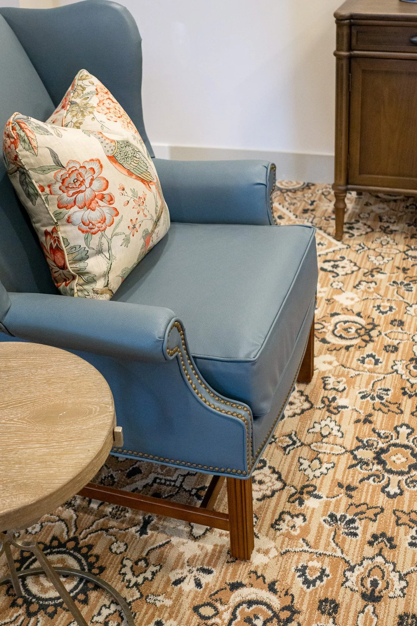 Senior living interior detail: overhead view of a blue leather wing chair with a floral pillow on a patterned rug