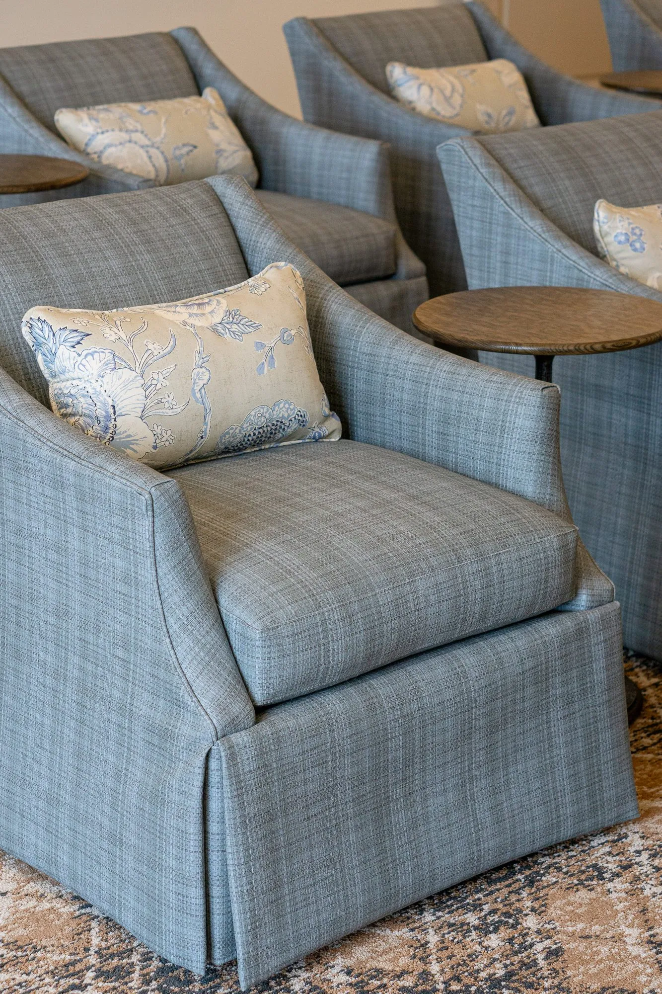 Senior living interior detail: skirted blue plaid armchairs with cream floral pillows and drink tables