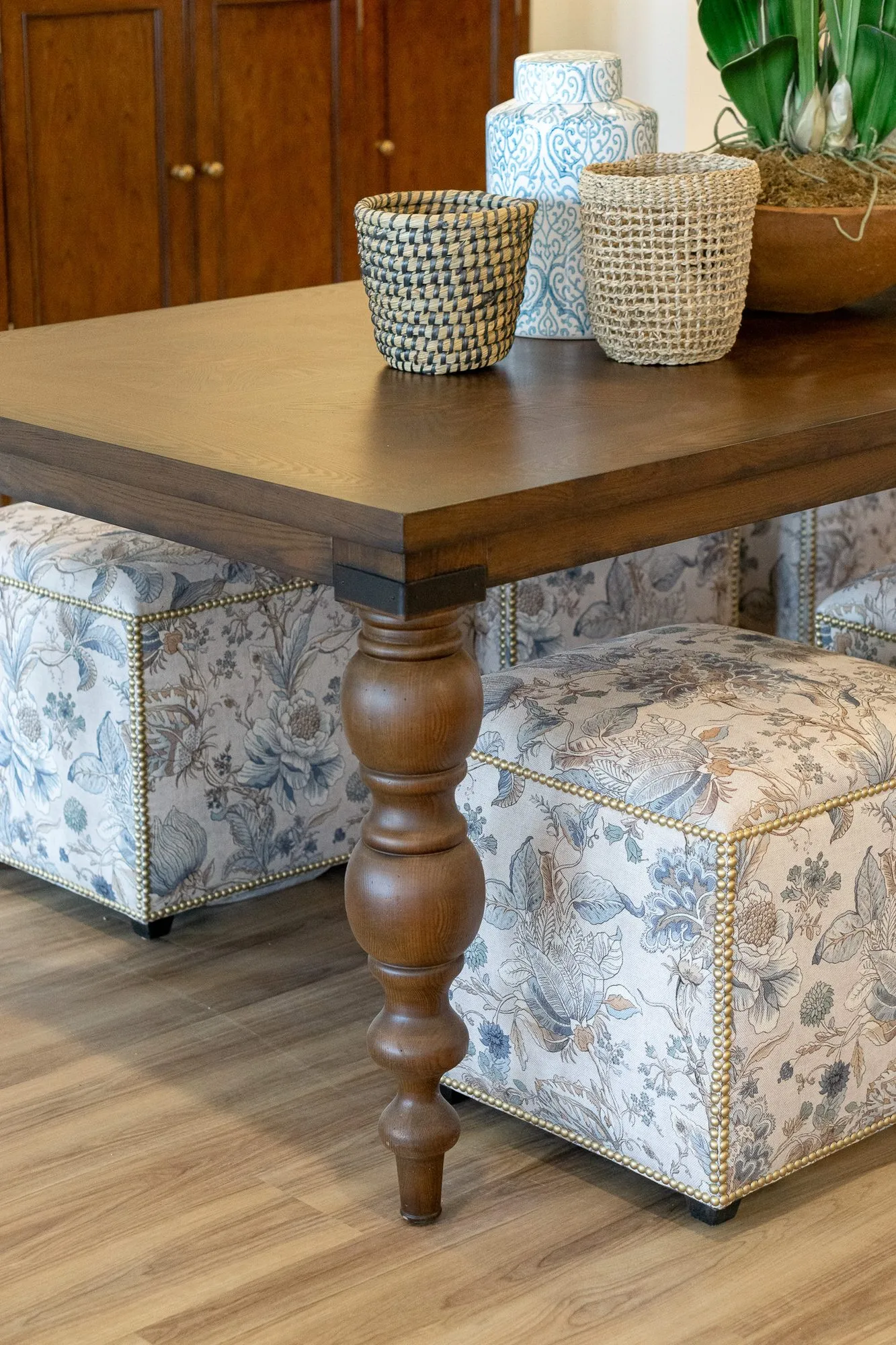 Senior living interior detail: turned walnut table leg among floral ottomans, baskets and a ceramic jar on top