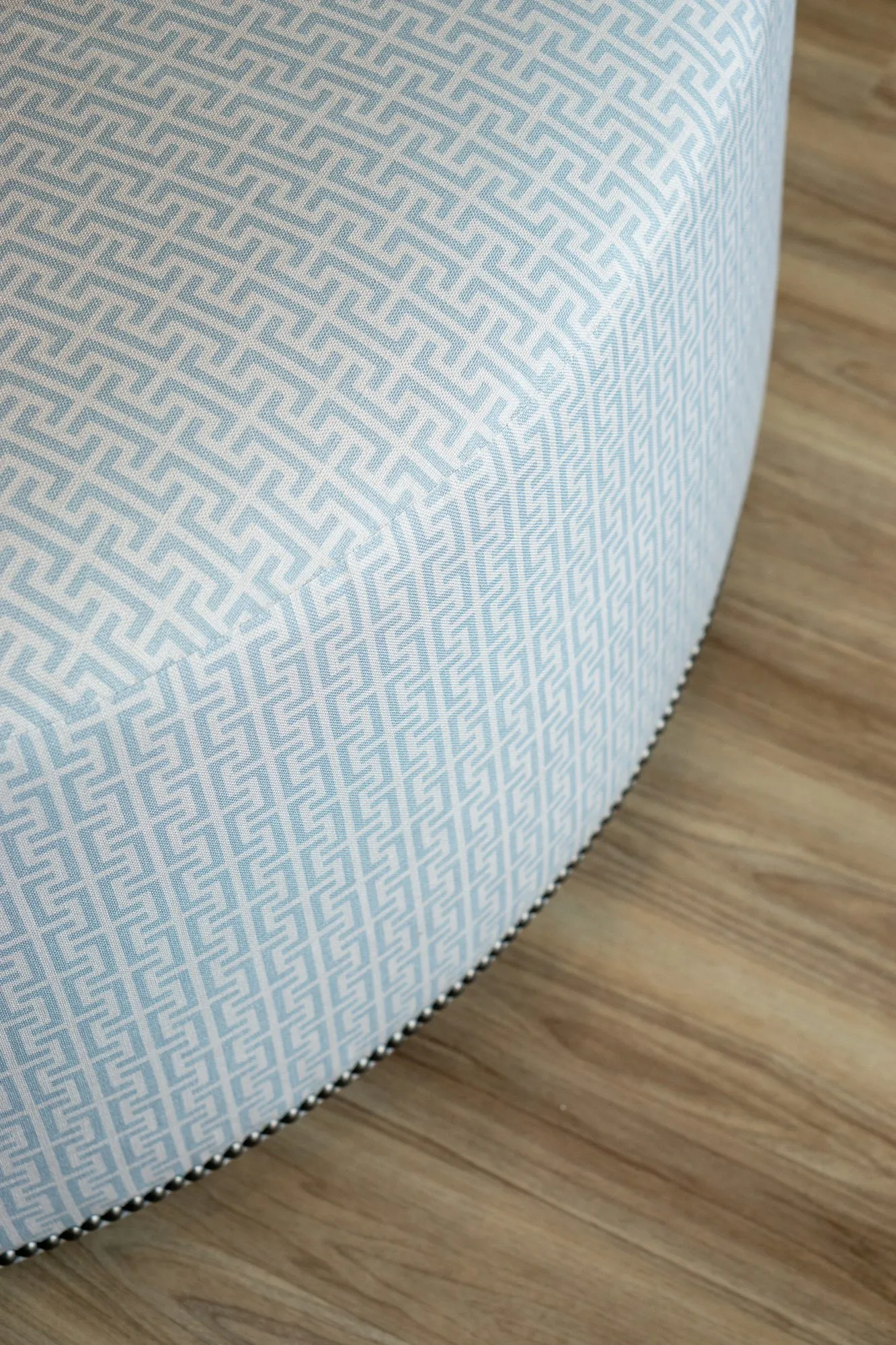 Senior living interior detail: round ottoman in pale blue fretwork fabric with a nailhead base