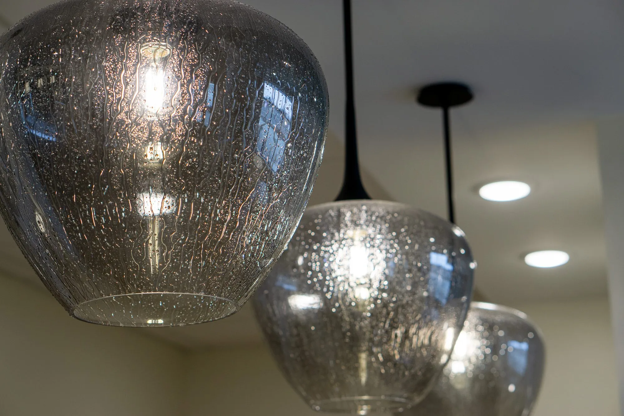 Senior living interior detail: three smoked seeded glass pendants hanging from black stems