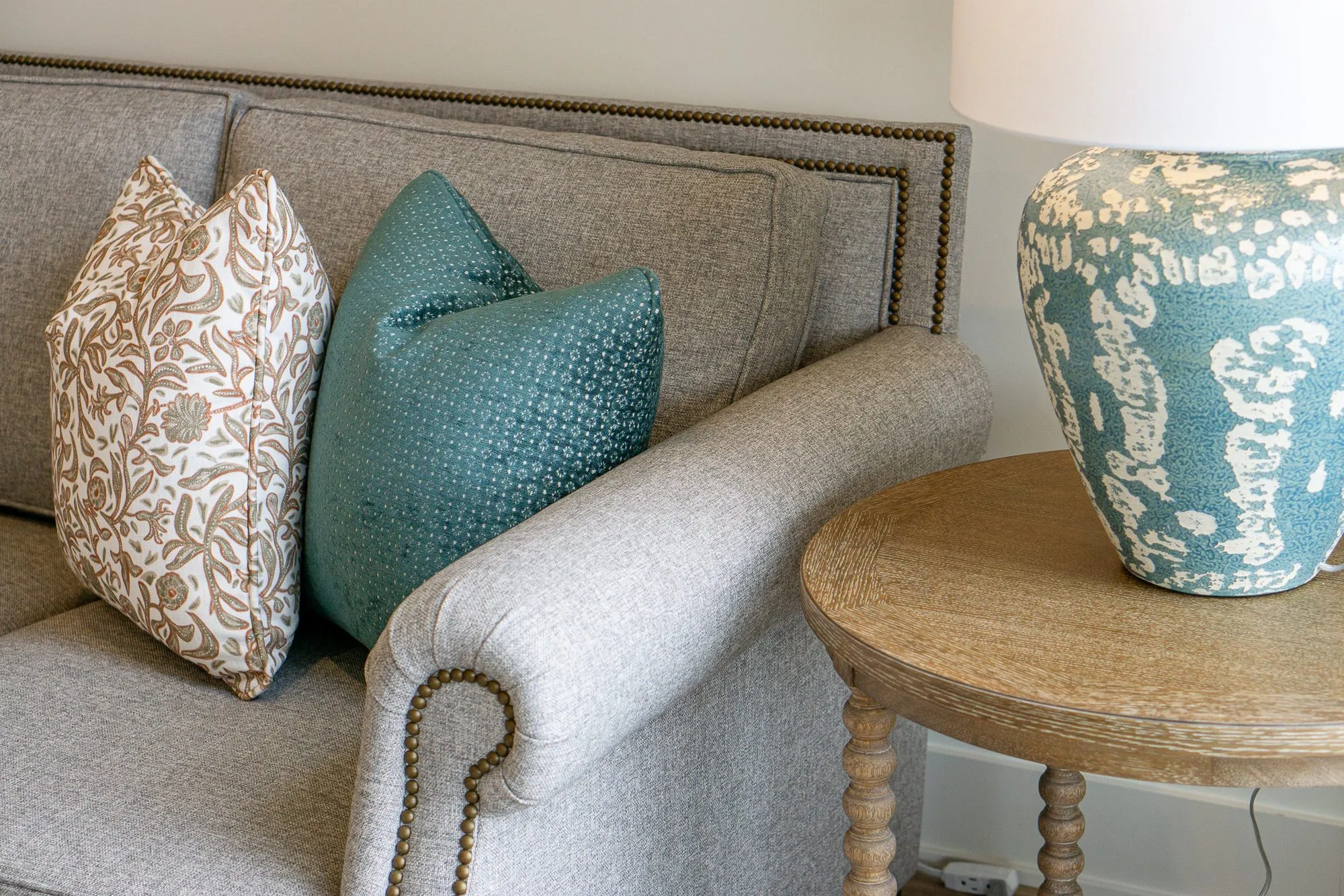 Senior living interior detail: patterned and teal pillows on the grey sofa beside a crackle glazed blue lamp base